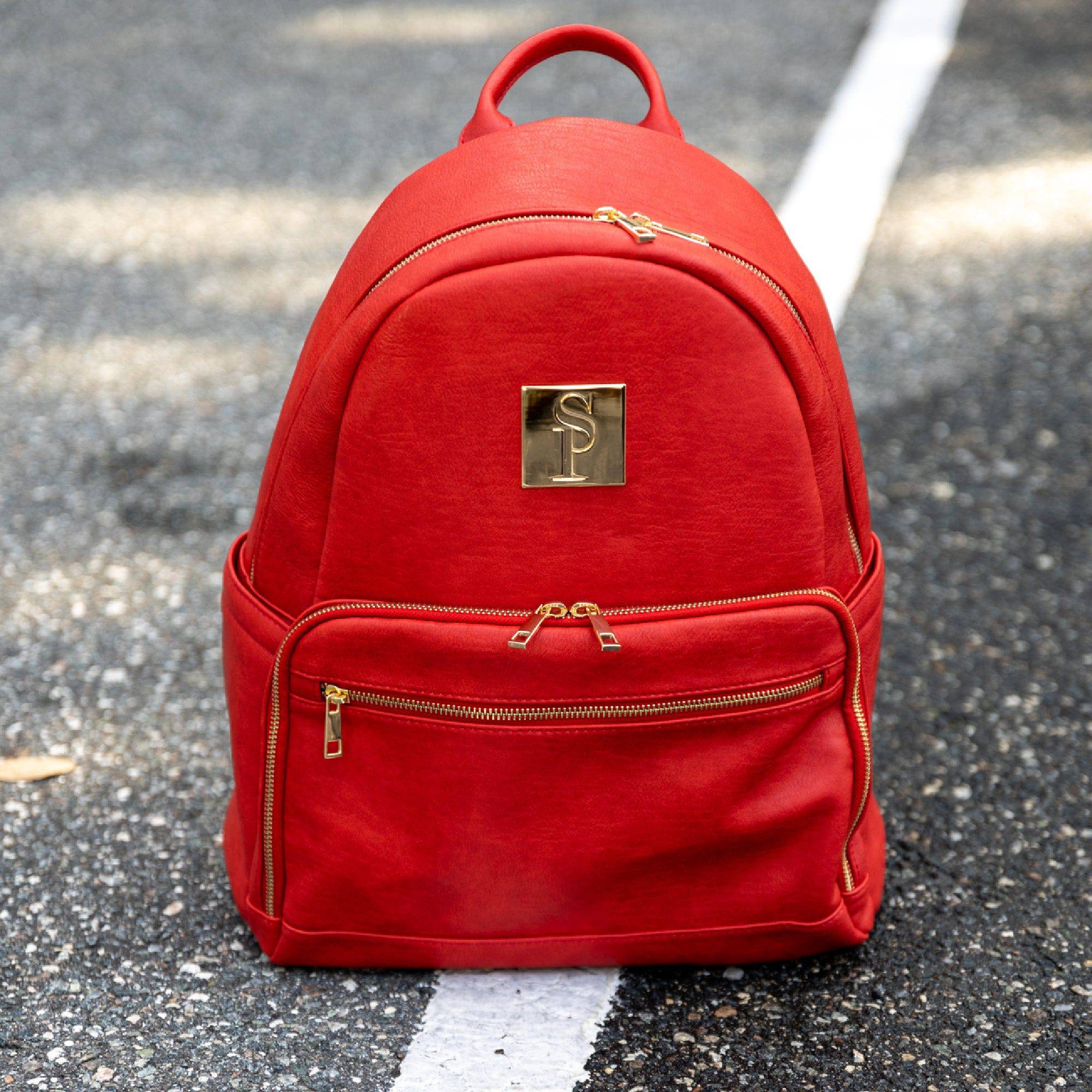 Red backpack with a gold logo on a road surface