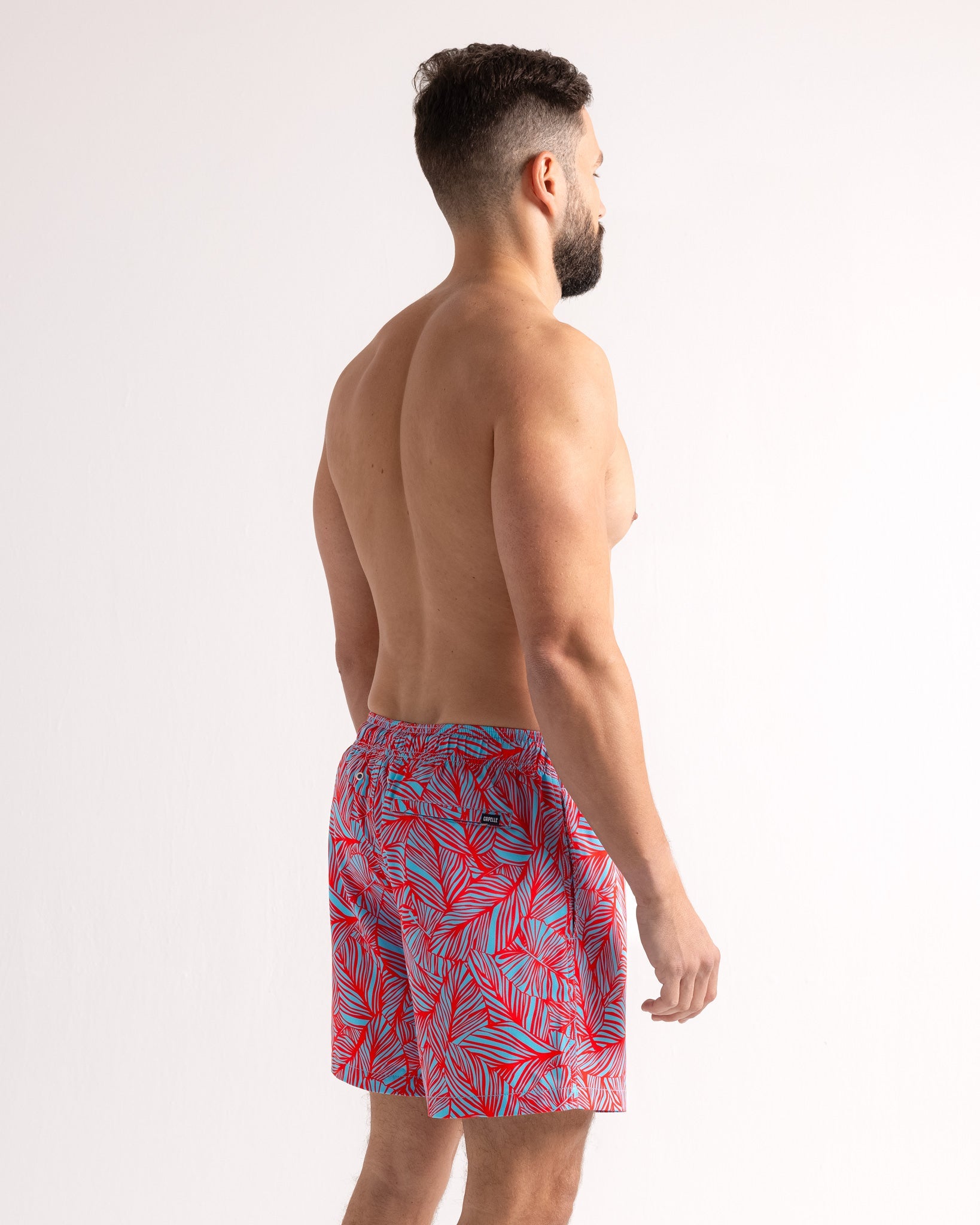 Man wearing red and blue patterned swim shorts on a white background