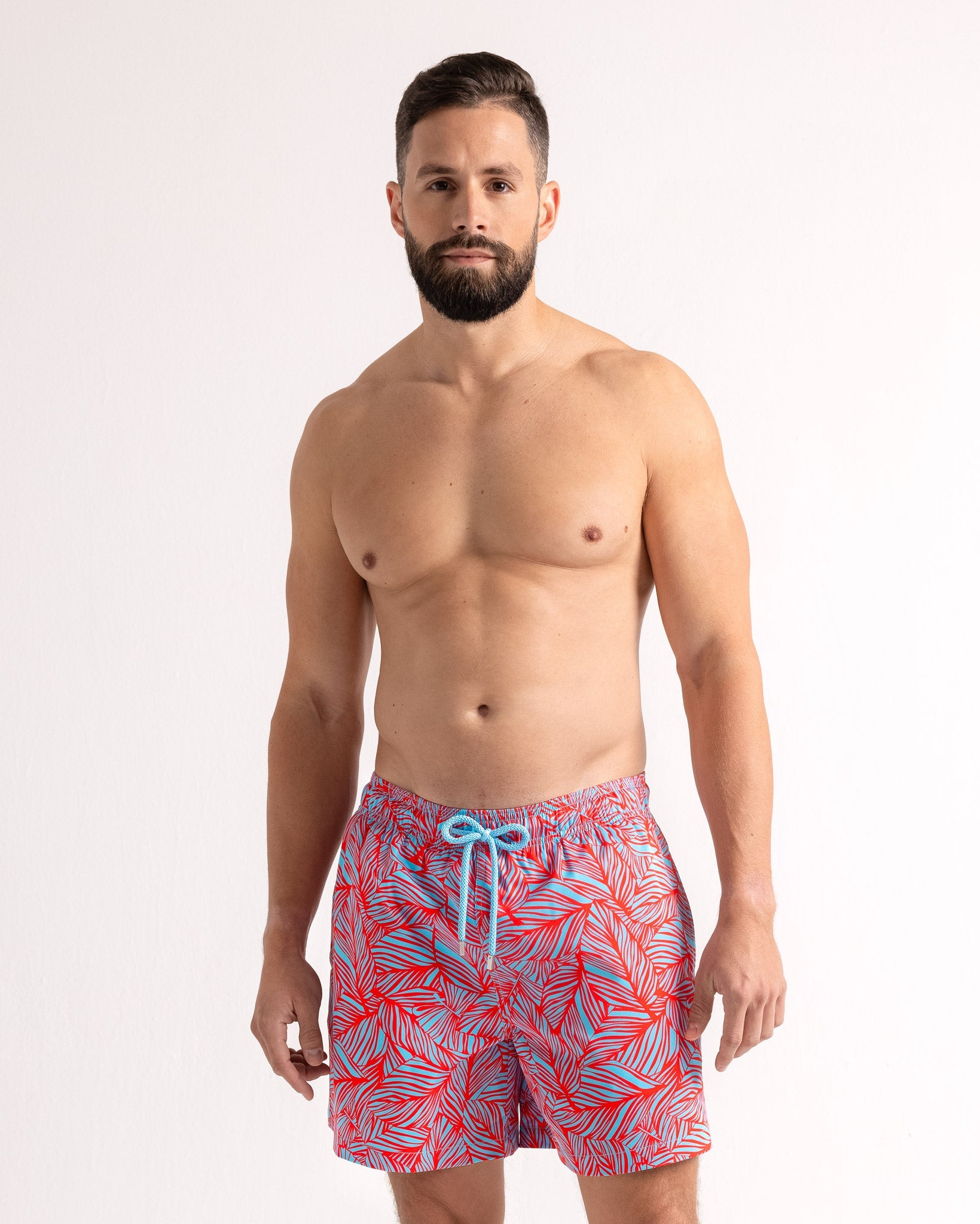 Man wearing red and blue patterned swim shorts on a white background