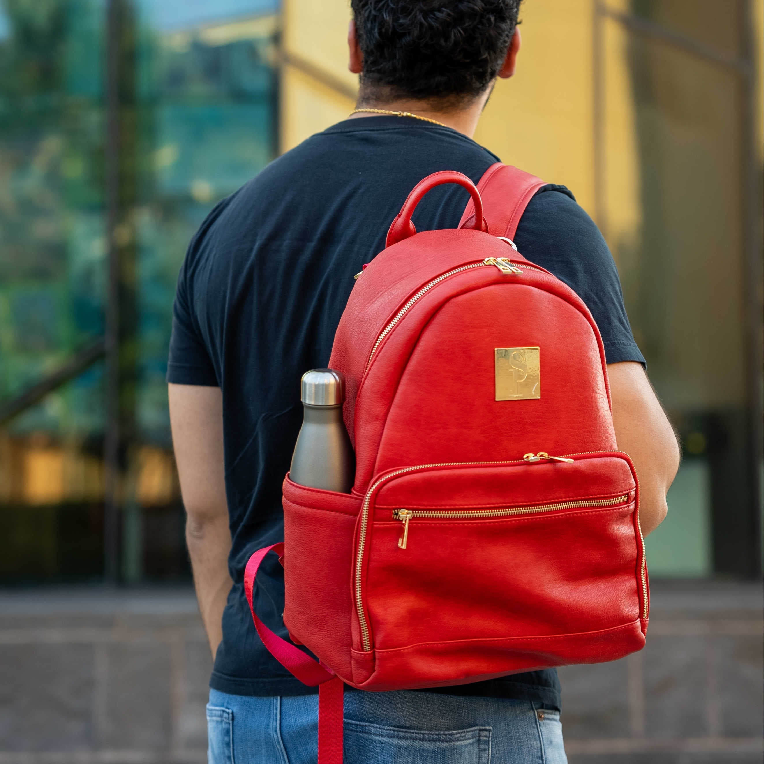 Person wearing a red backpack with a water bottle, standing in front of a blurred background