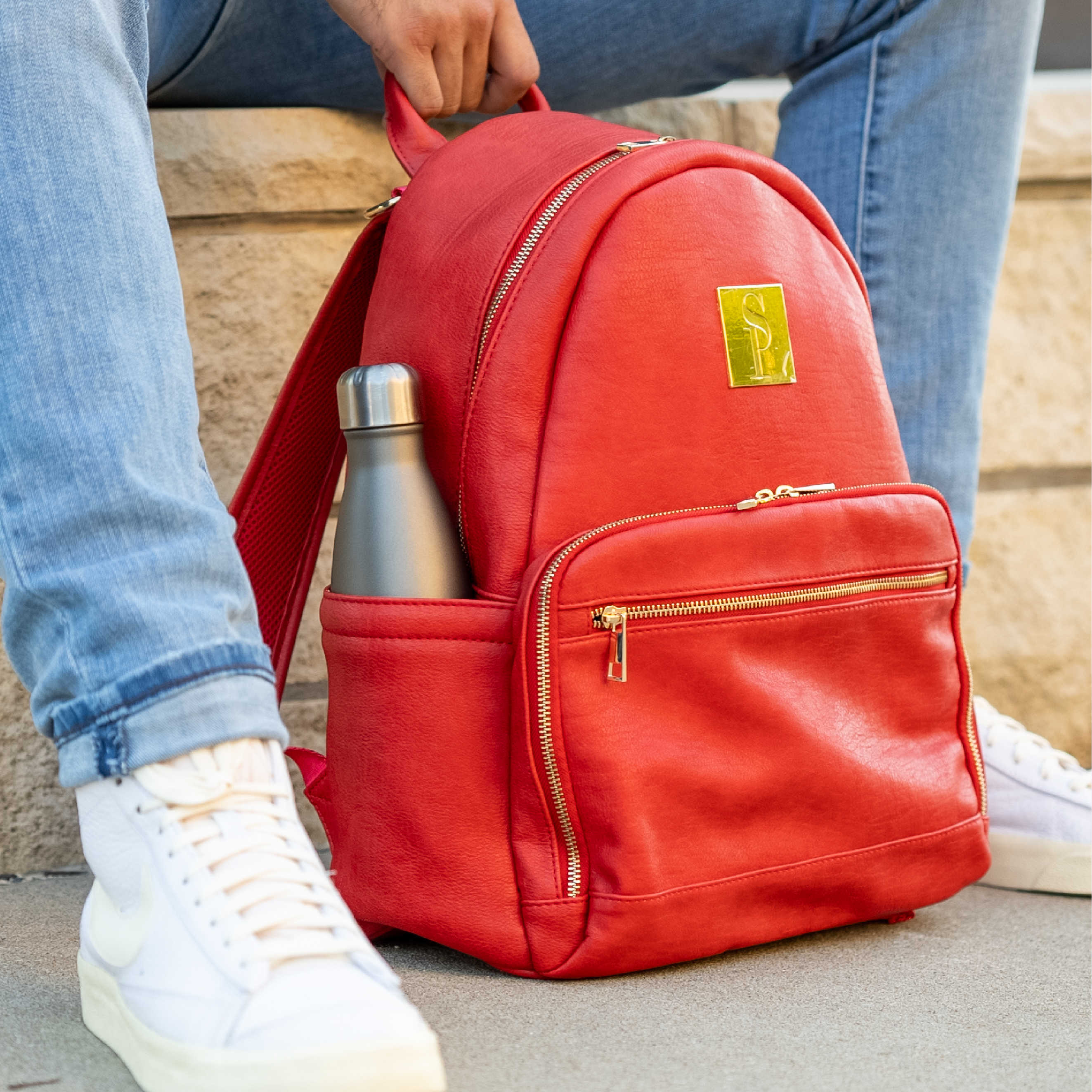 Red backpack with a water bottle on a stone surface