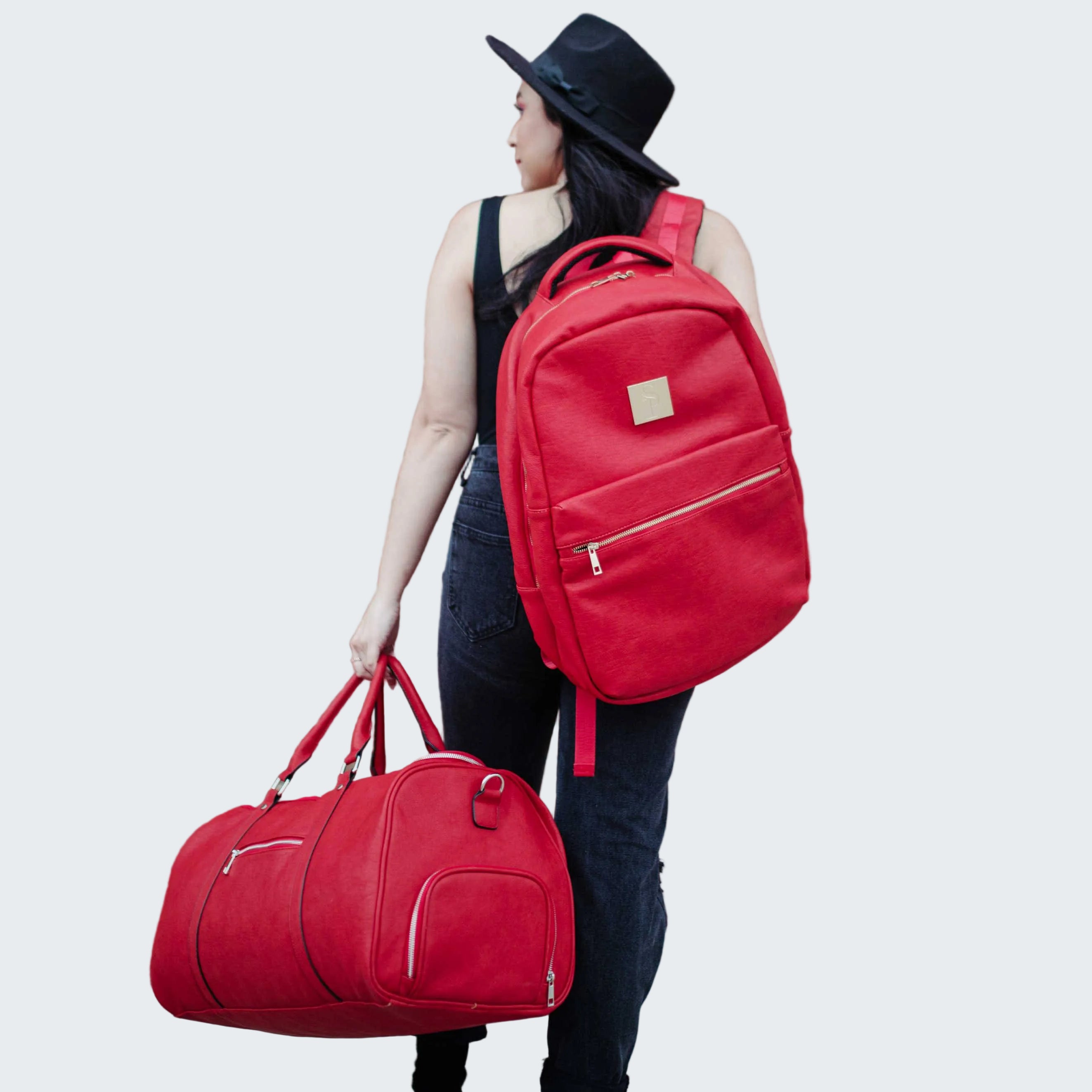 Person holding a red backpack and duffel bag against a brick wall.