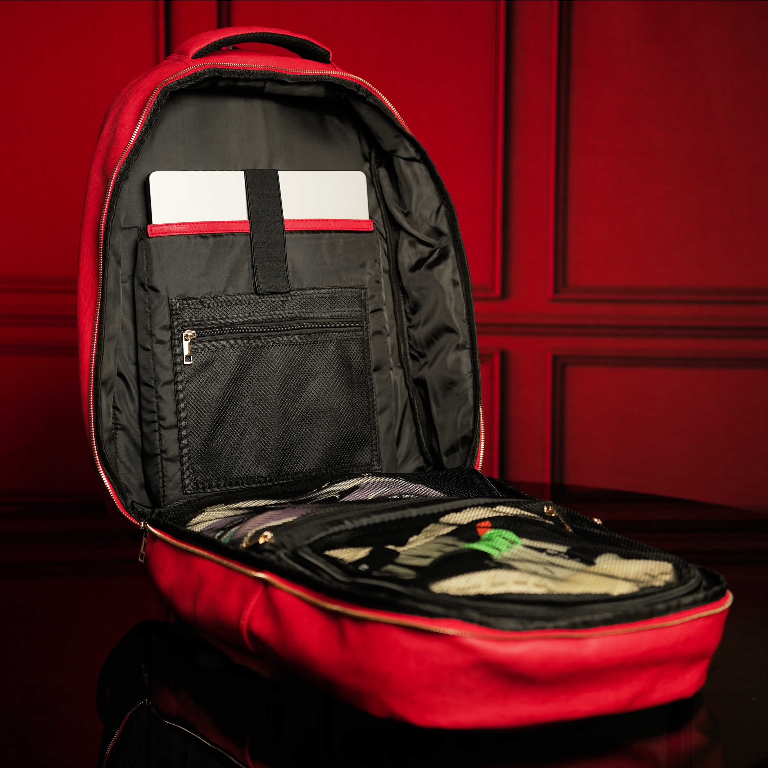 Red backpack with open compartment against a red wall