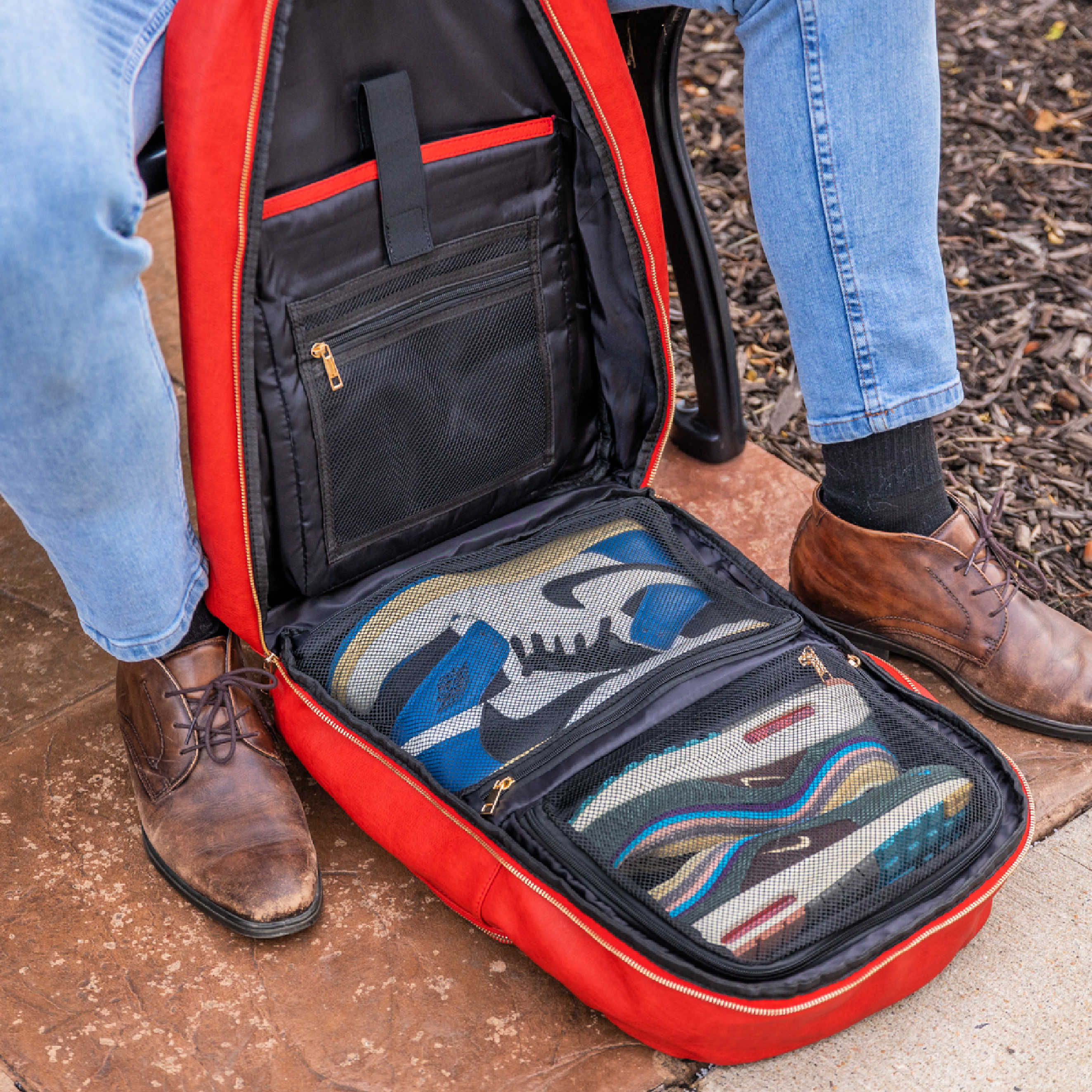 Red backpack with a compartment containing shoes, worn by a person on a stone surface.