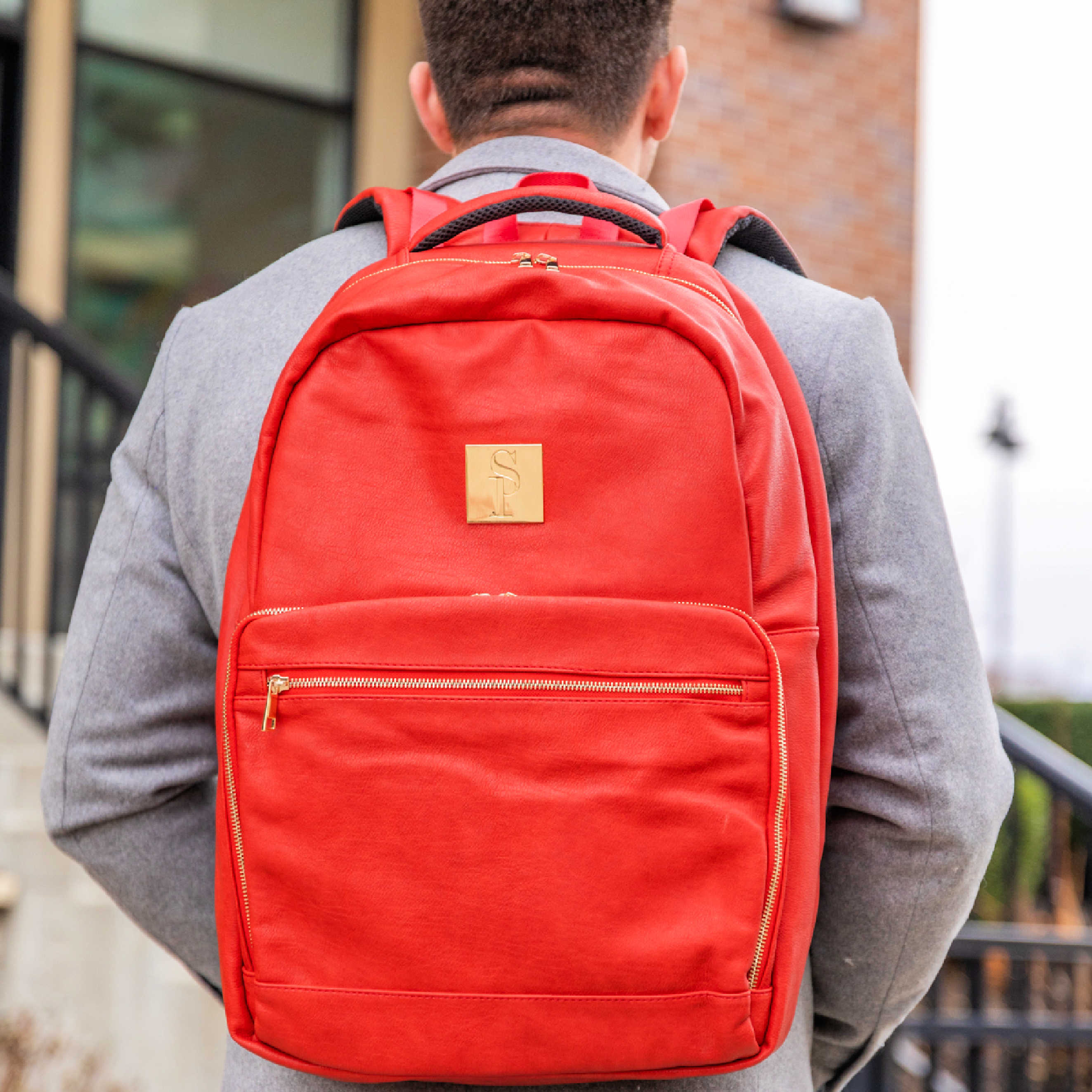 Person wearing a red backpack with a gold tag outdoors.