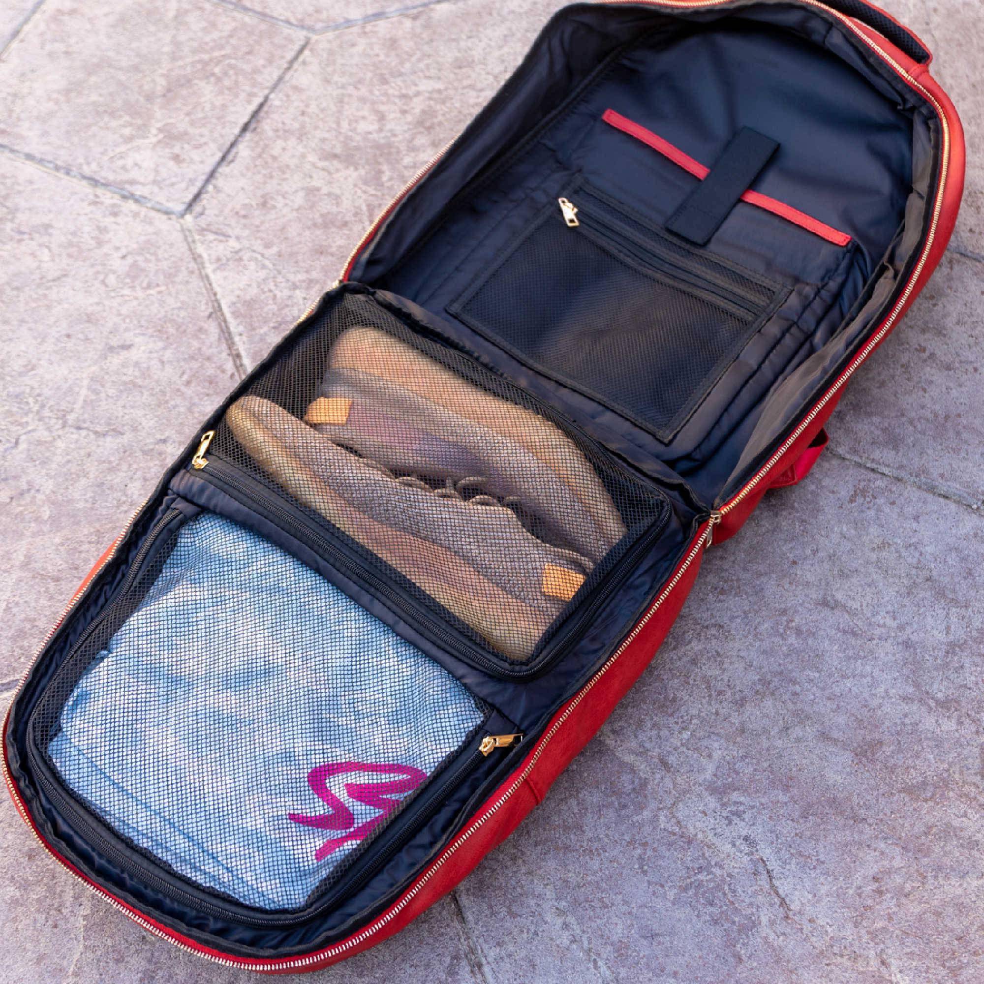 Open red travel bag with shoes and packing cubes on a stone surface