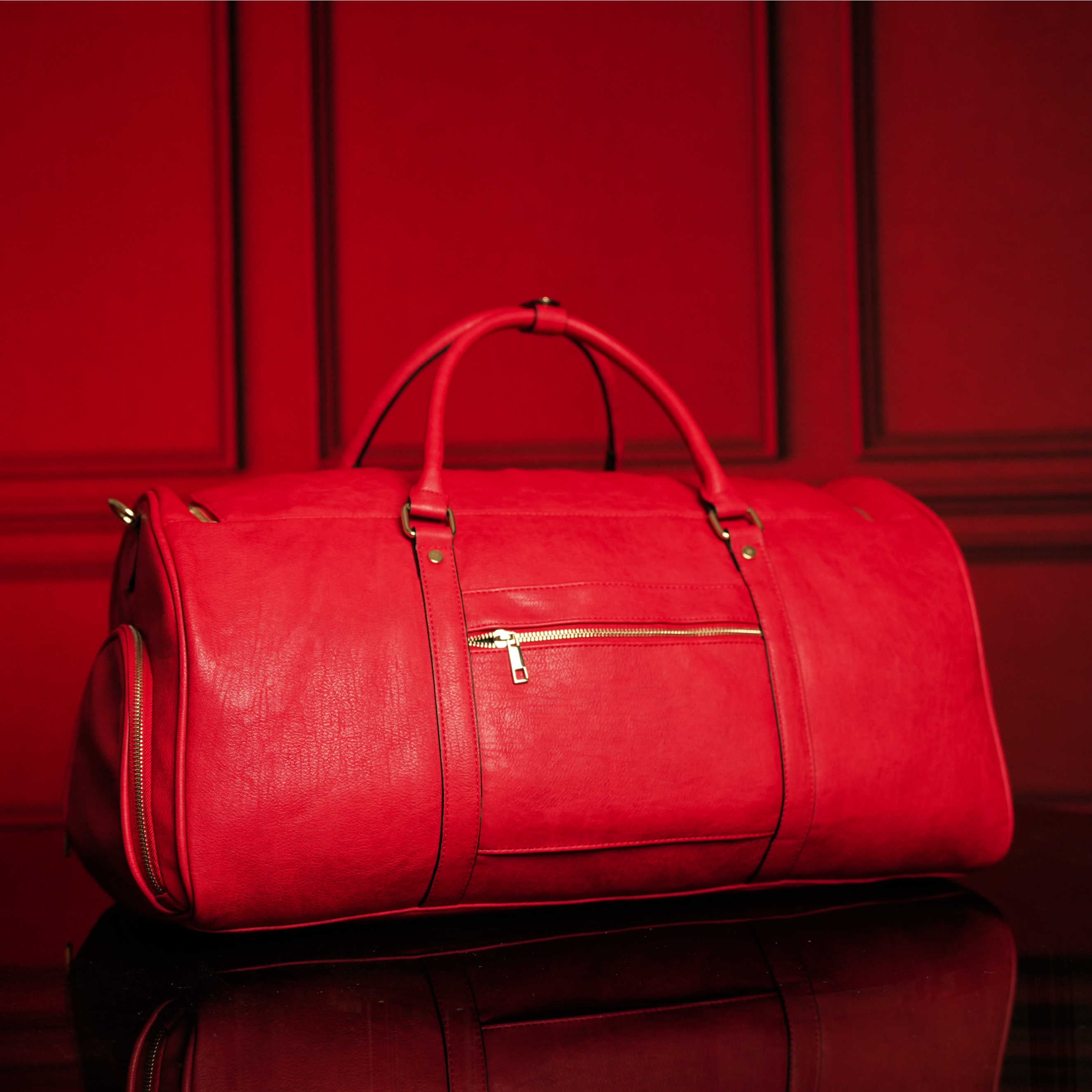 Red leather duffel bag on a reflective surface with a red background