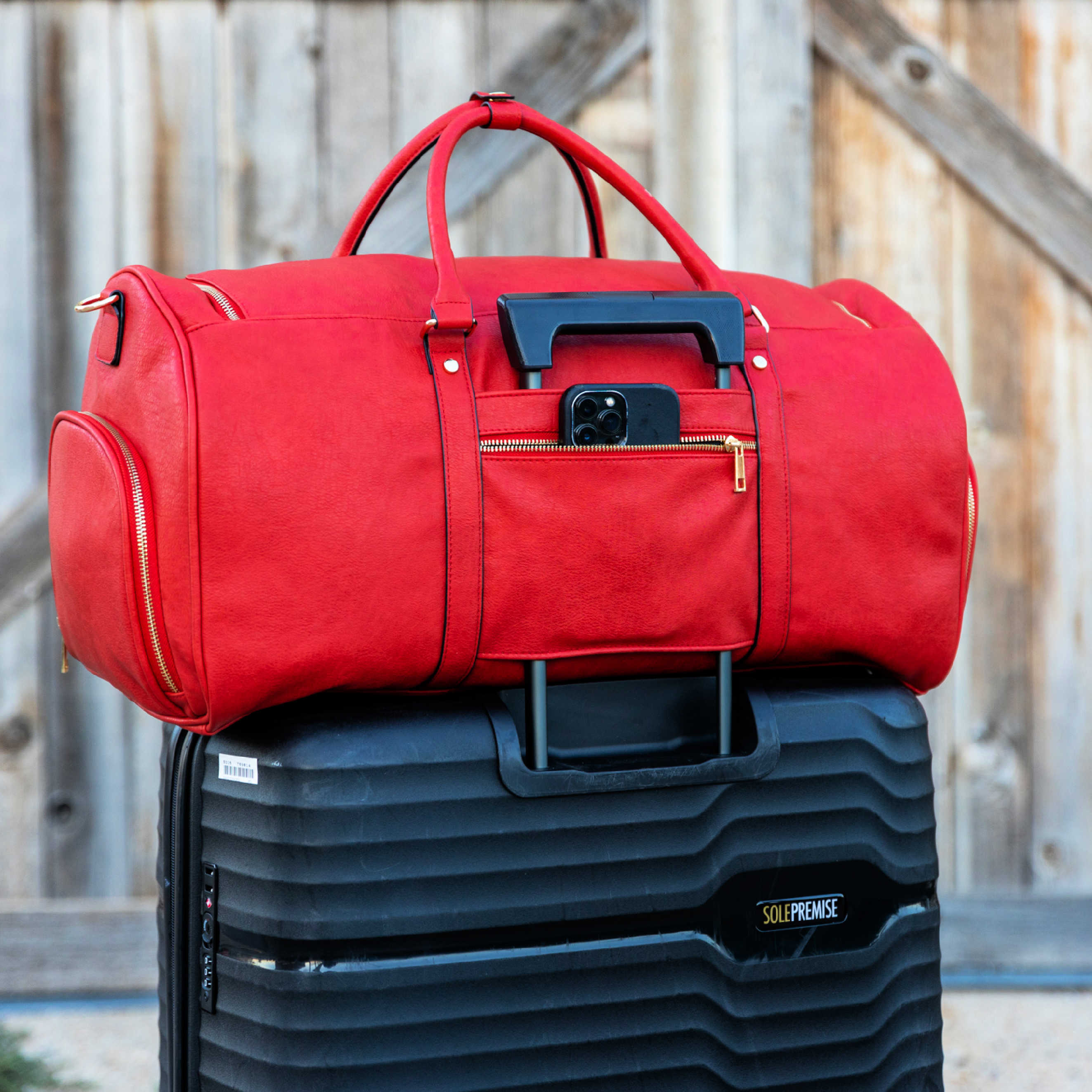 Red duffel bag on top of a black suitcase with a wooden background