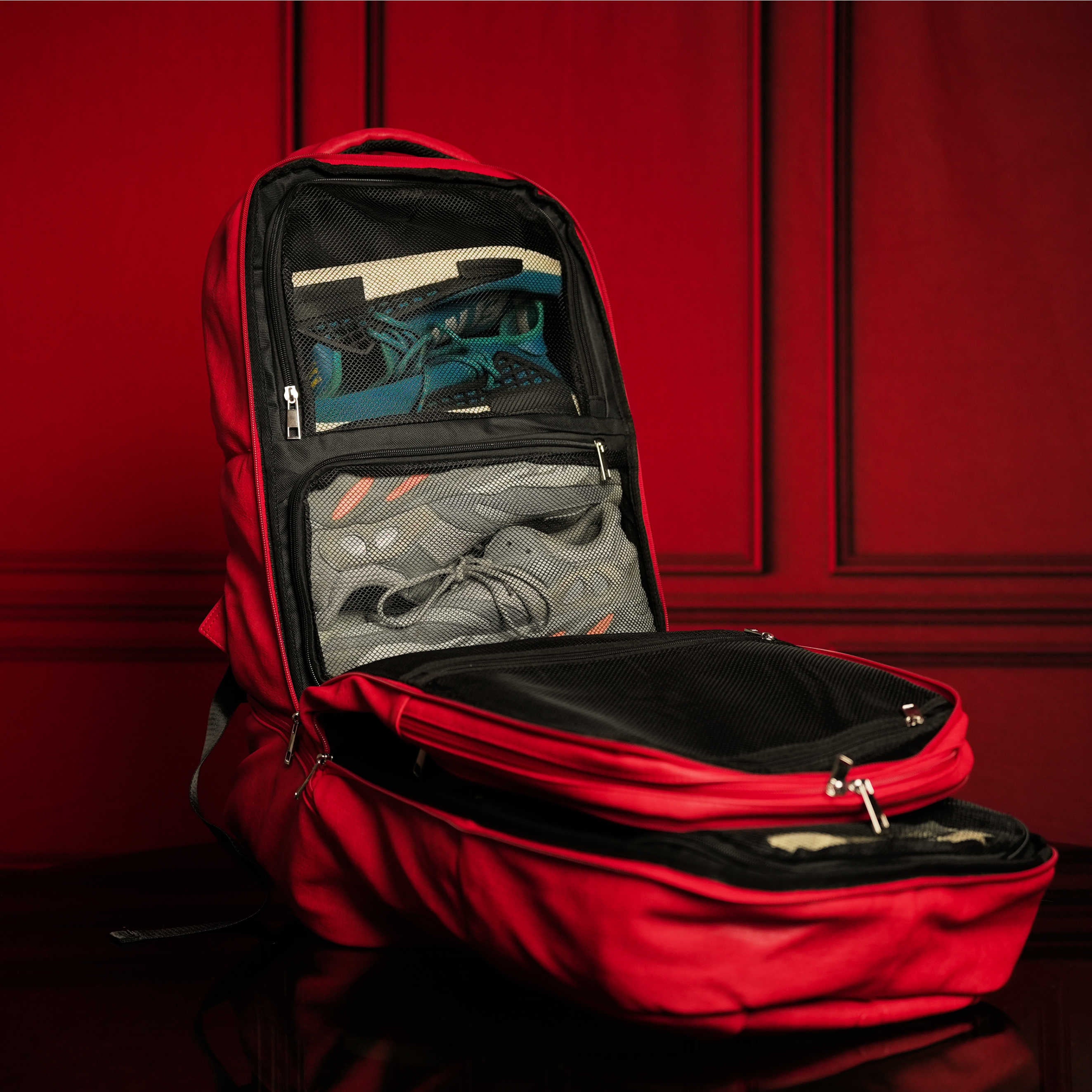 Red backpack with open compartments against a red background