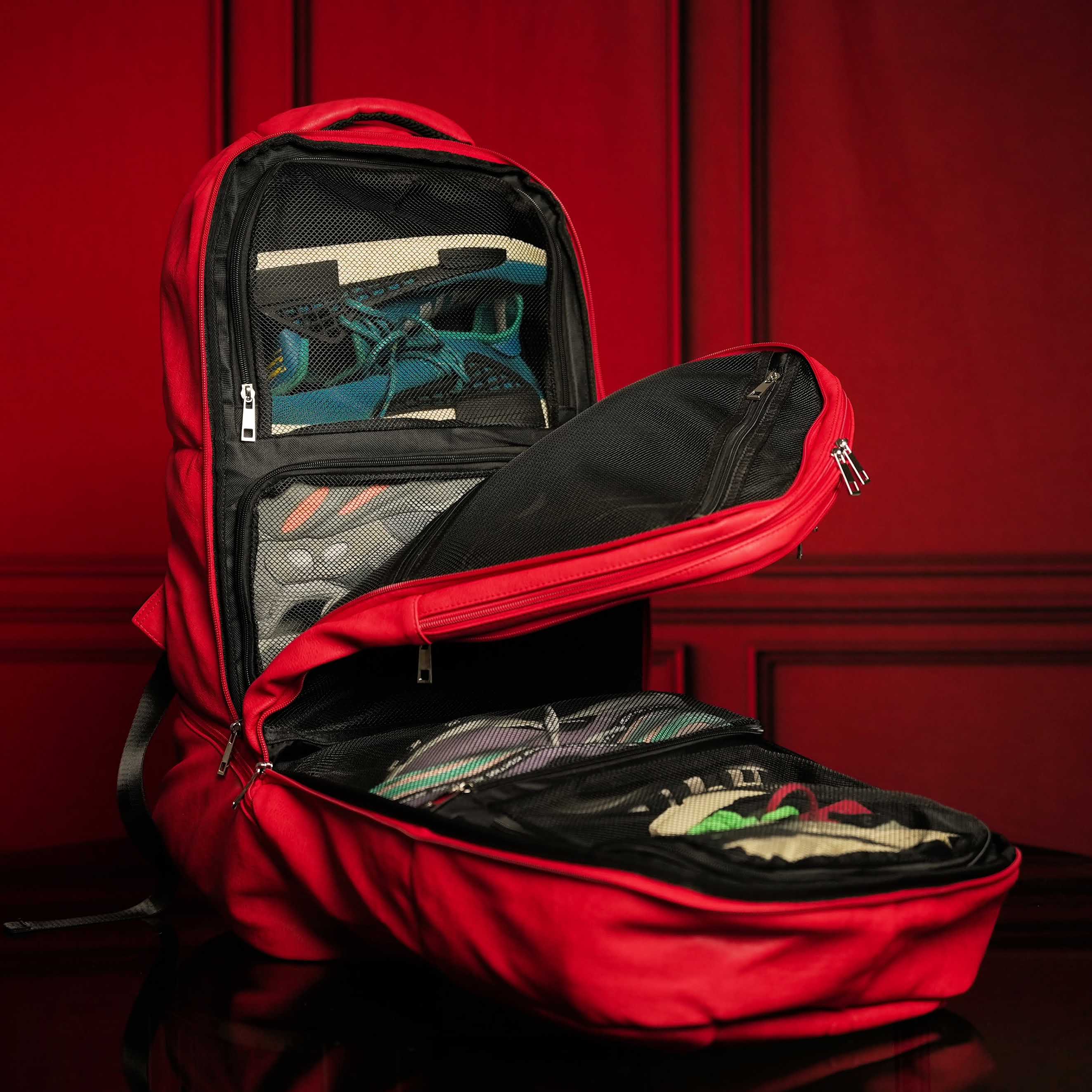 Red backpack with open compartments displaying various items against a red background