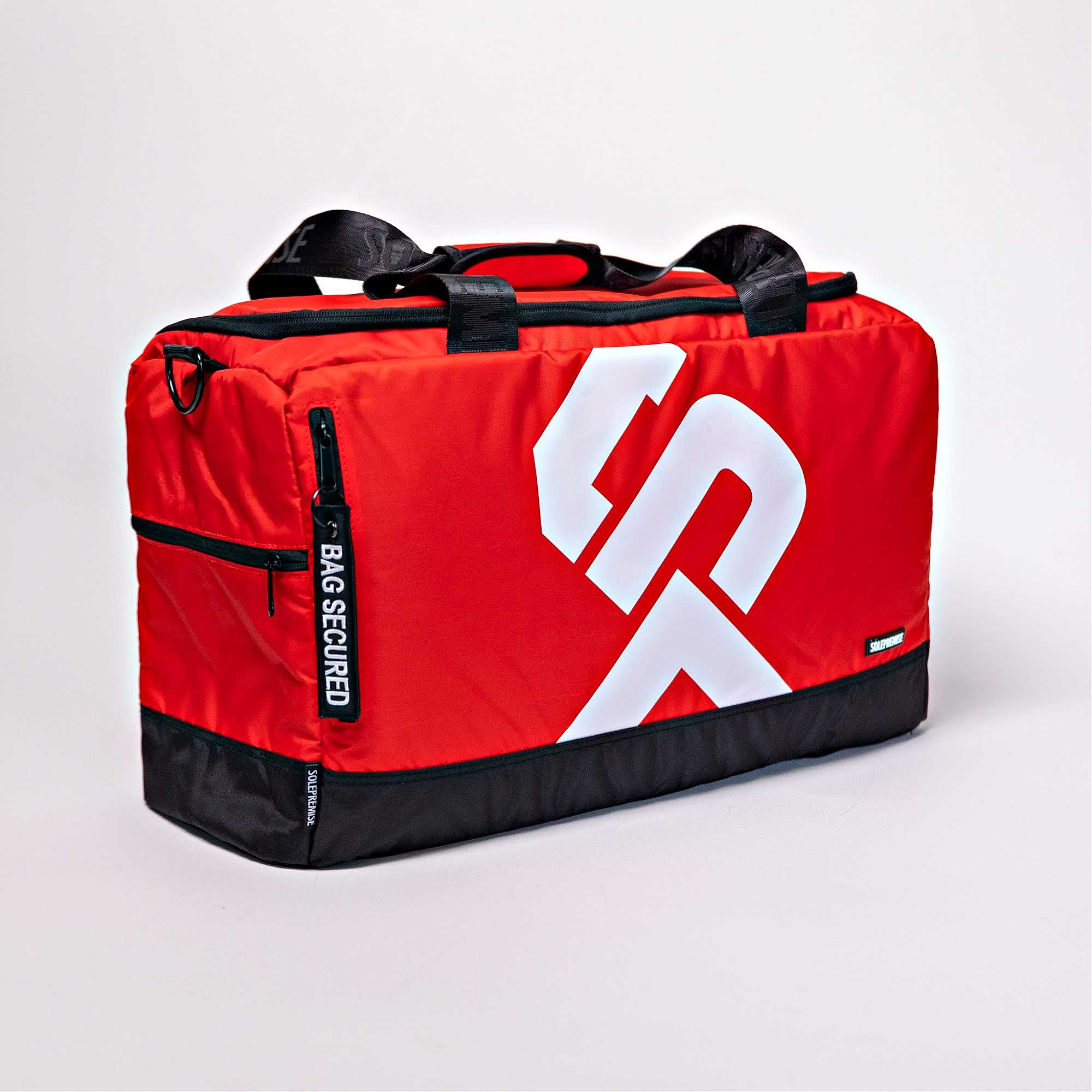 Red duffel bag with black accents and a white logo on a light gray background