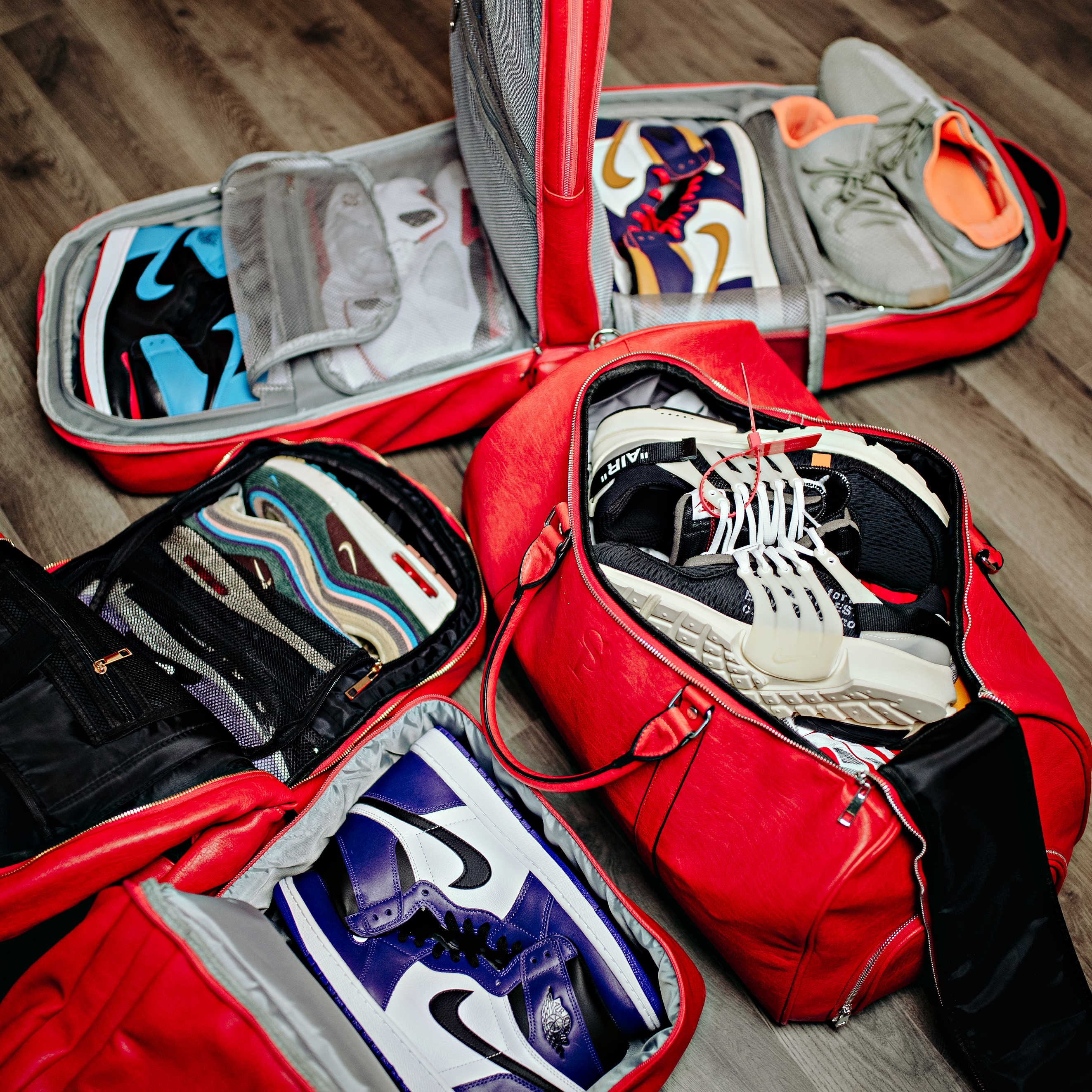Red duffel bag with various pairs of sneakers inside on a wooden floor.