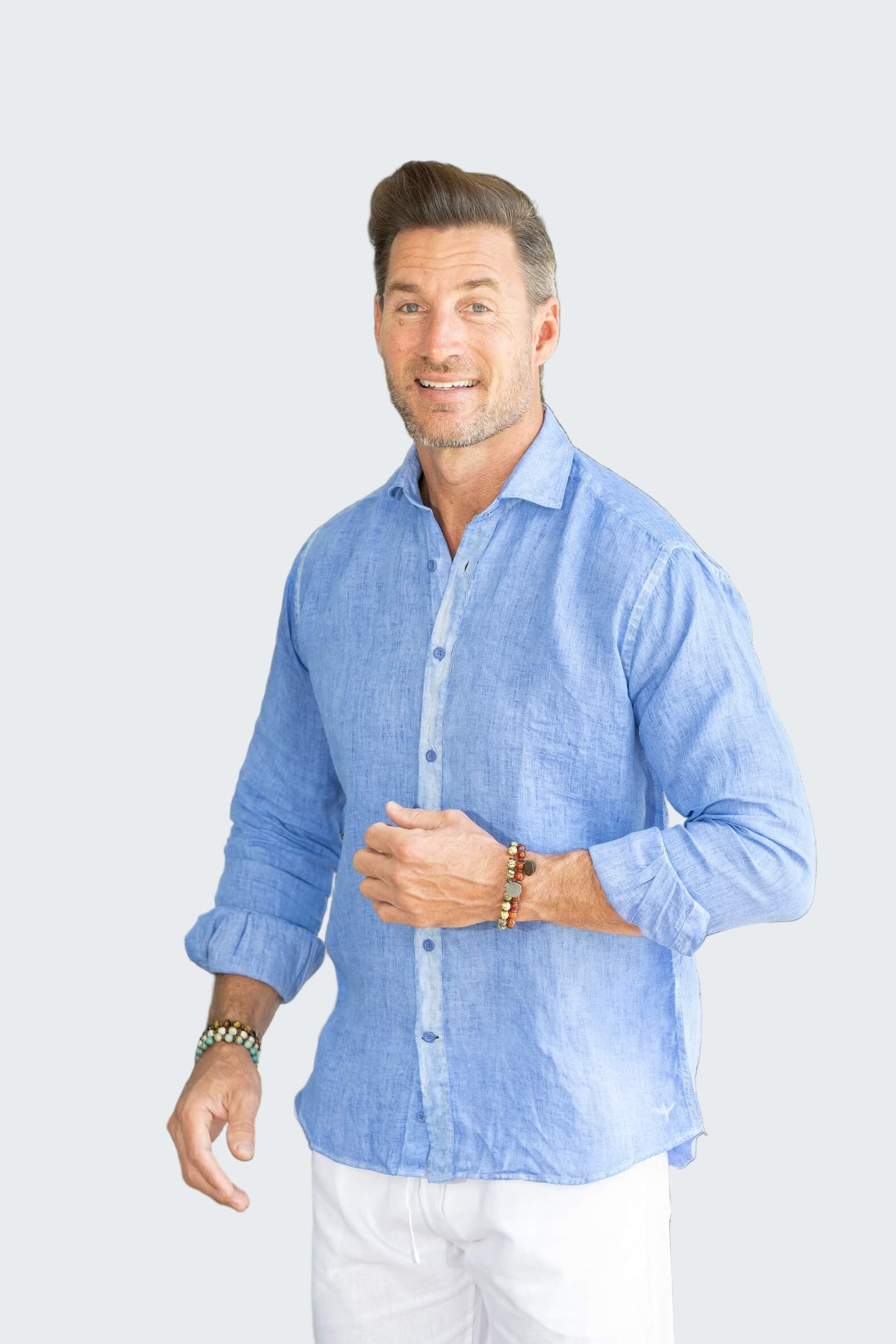 Man wearing a light blue shirt and white pants standing outdoors with plants in the background