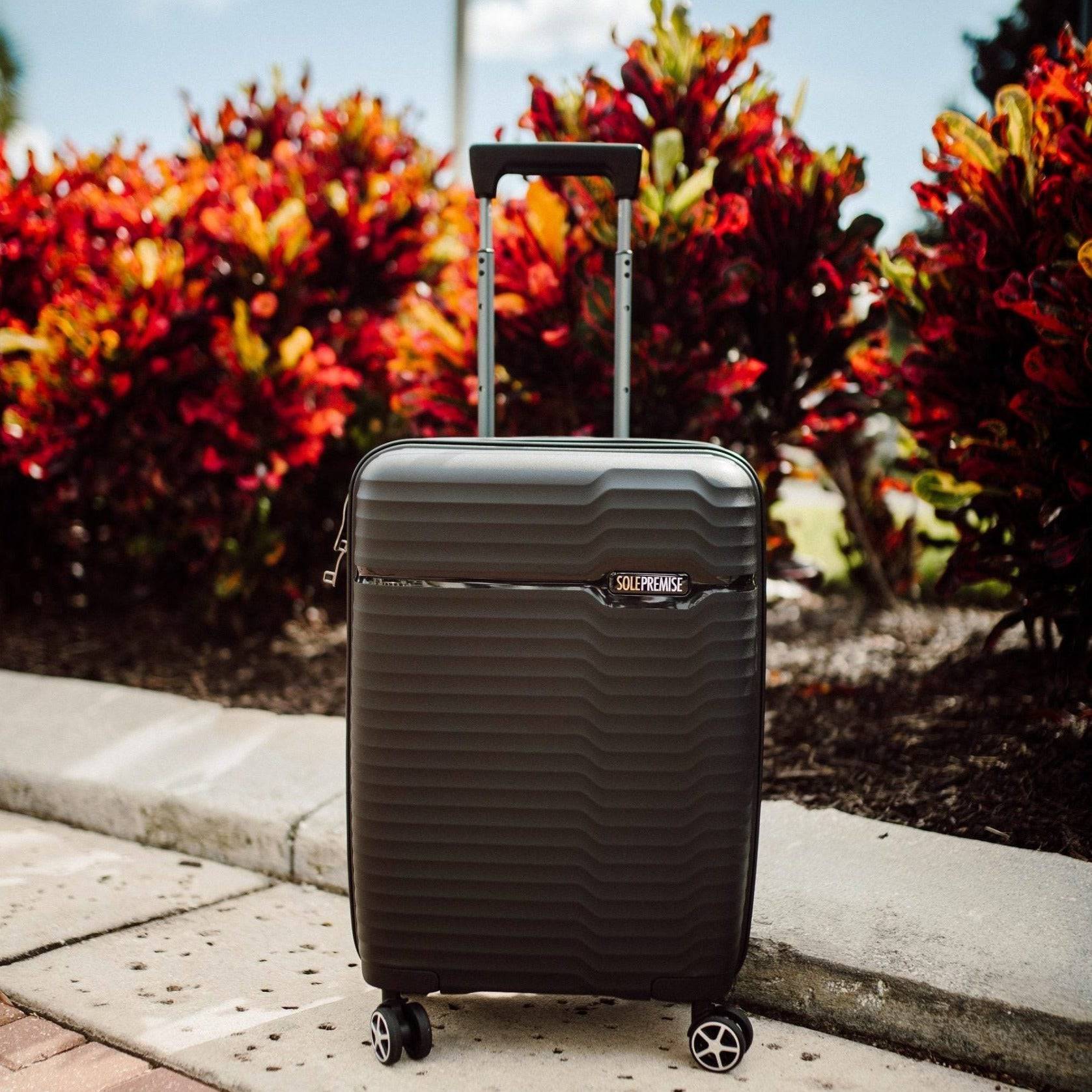 Black suitcase with 'Samsonite' logo on a sidewalk with colorful bushes in the background