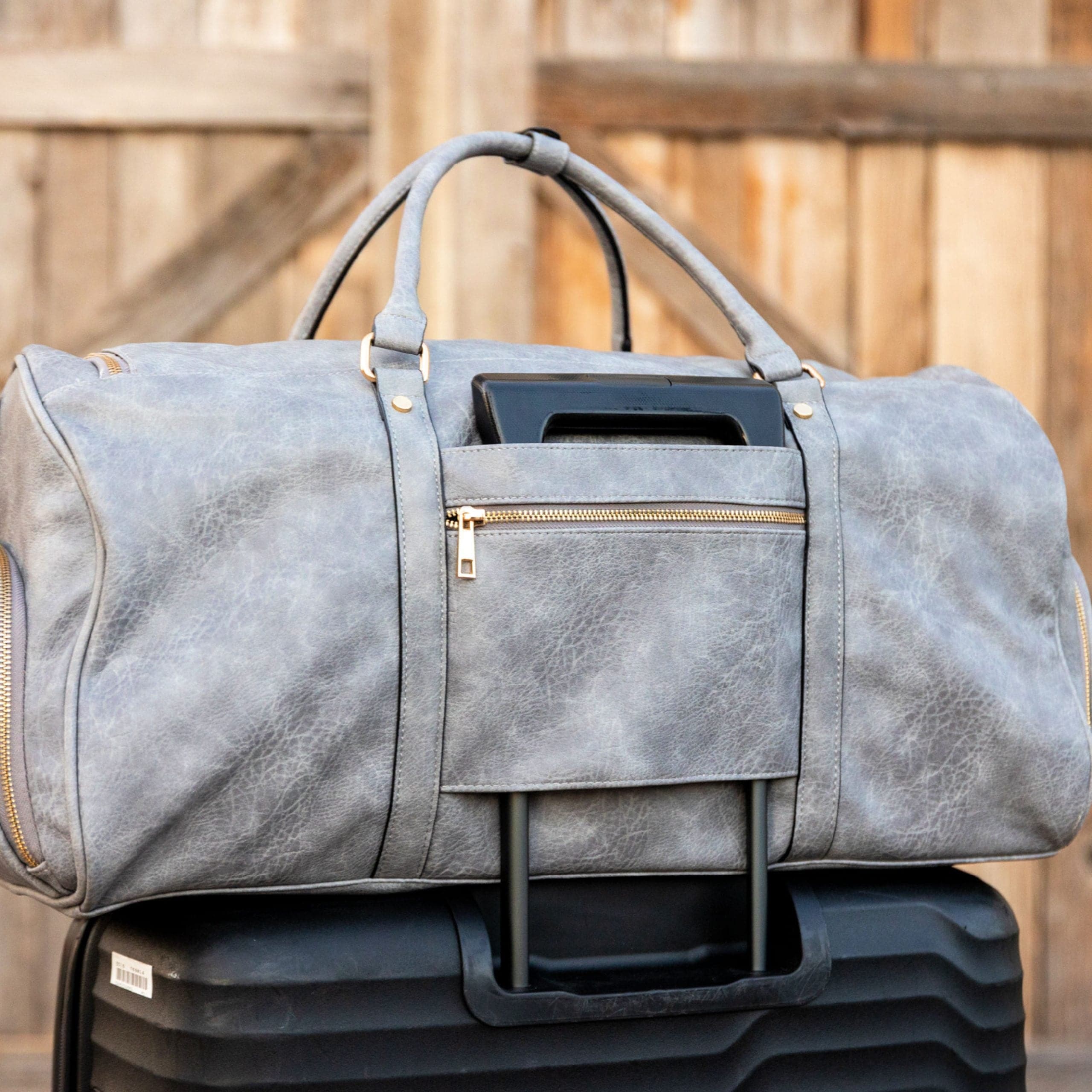 Gray duffel bag with gold zippers on a wooden surface
