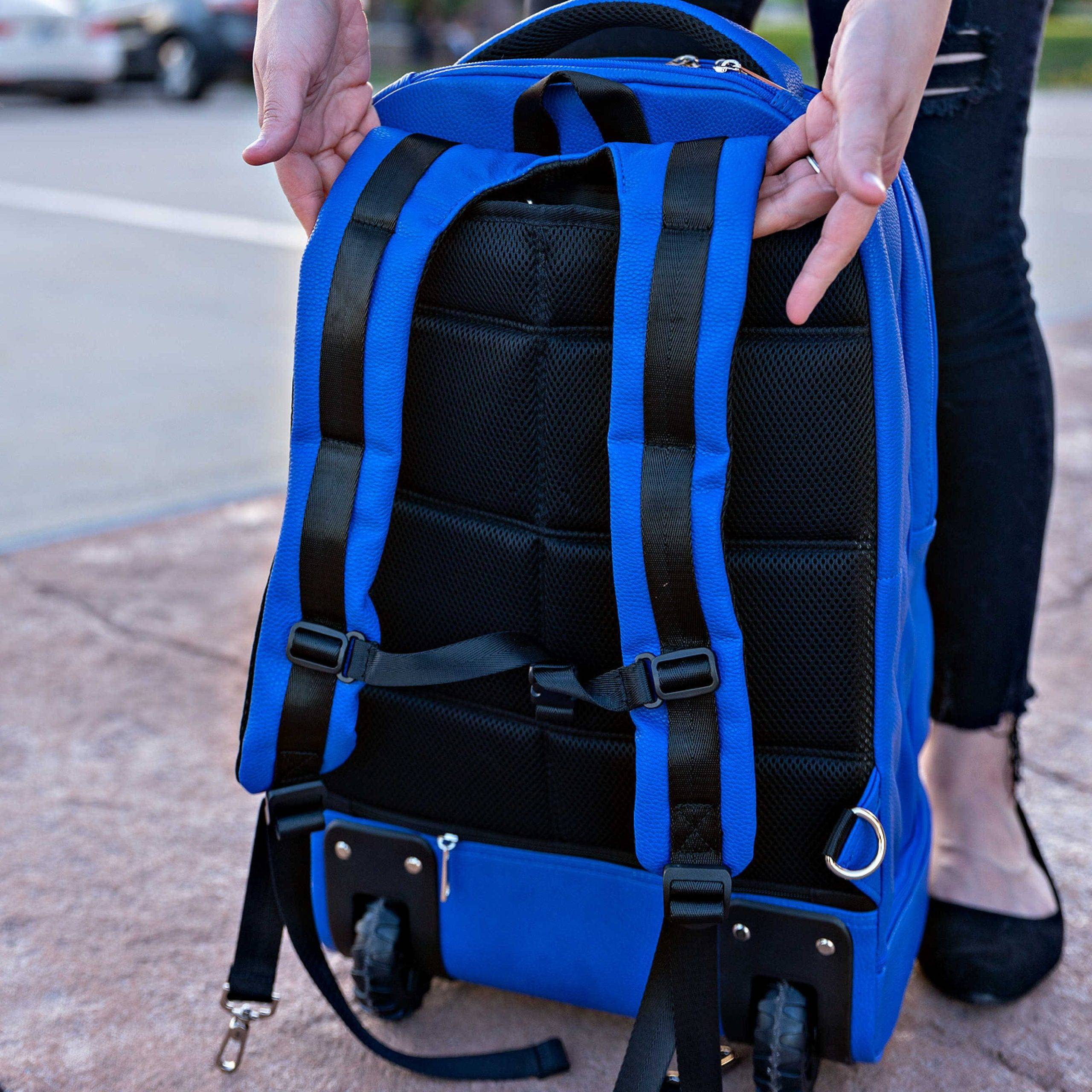 Blue backpack with black straps held by a person outdoors.