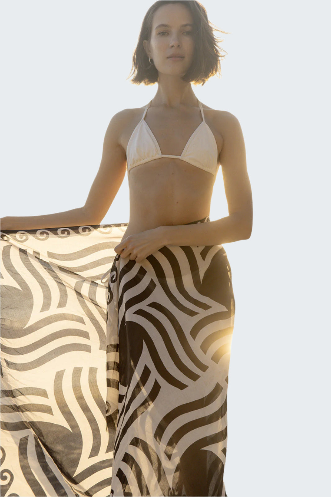 Woman in a bikini and patterned sarong standing on a beach.