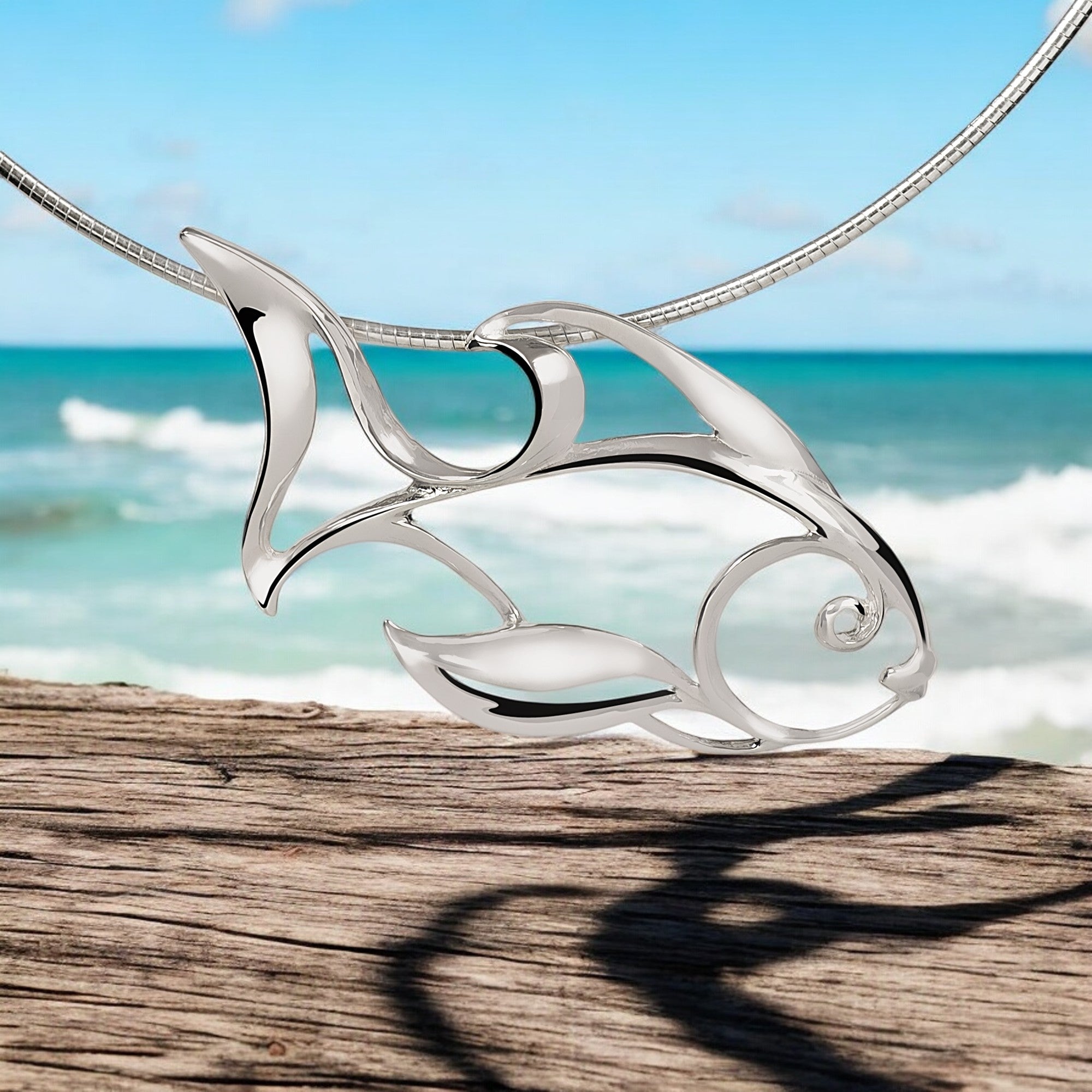 Silver fish-shaped pendant on a chain with a beach background