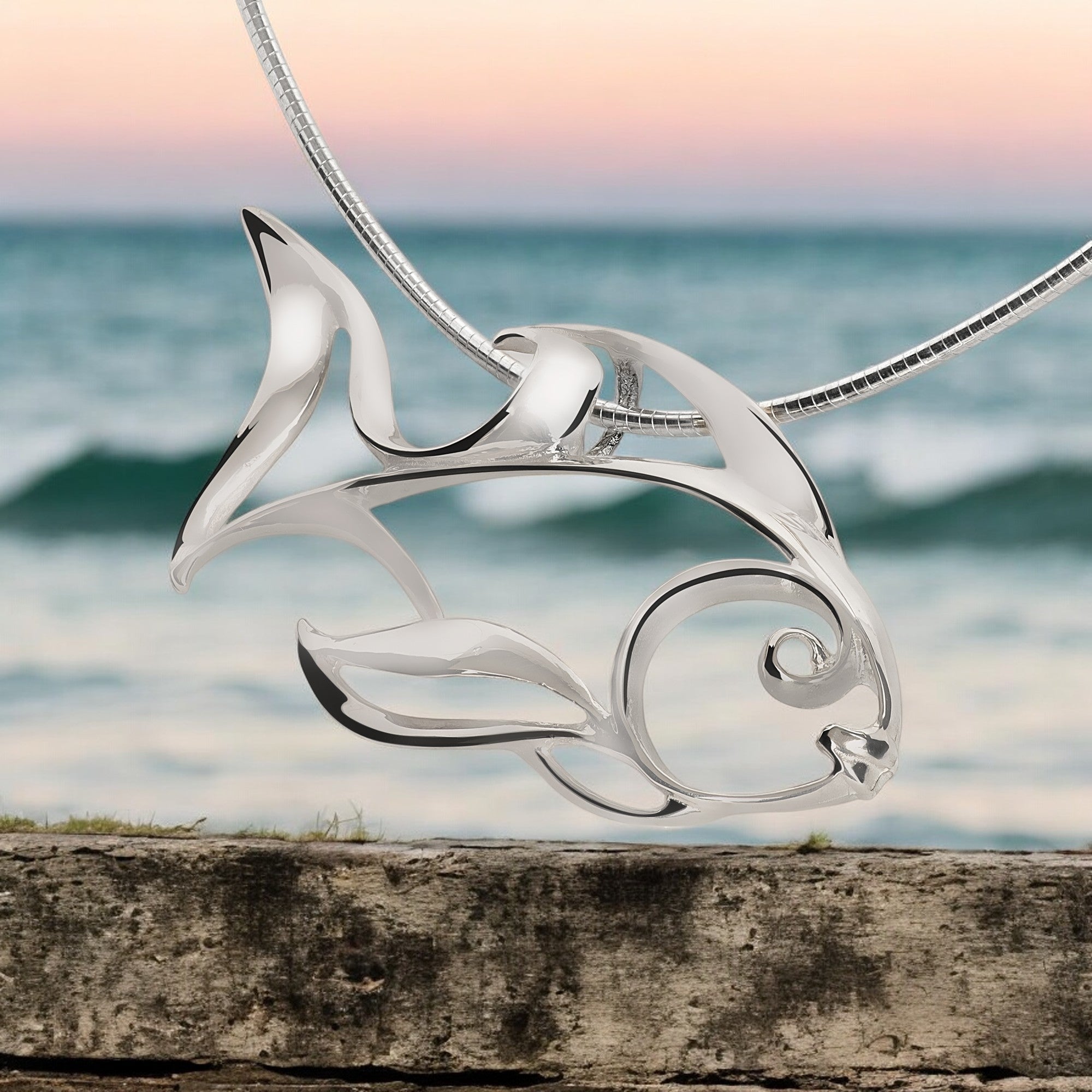 Silver dolphin pendant on a chain with a blurred ocean background