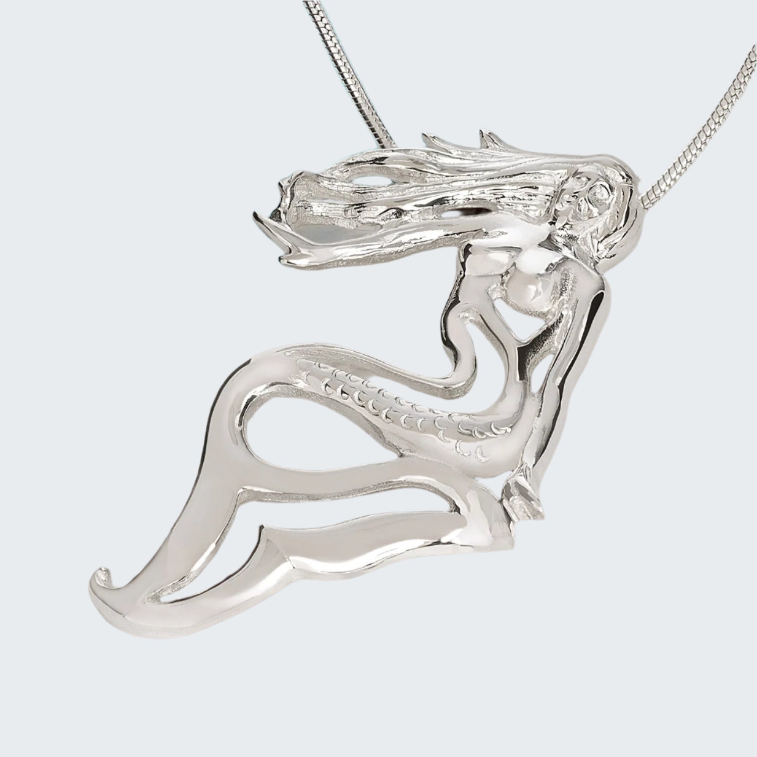 Silver dragon pendant on a wooden surface with a blurred turquoise background