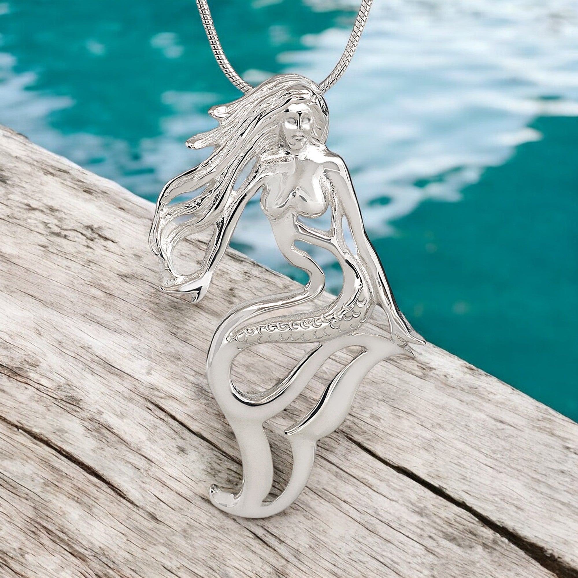 Silver mermaid pendant on a wooden surface with water in the background