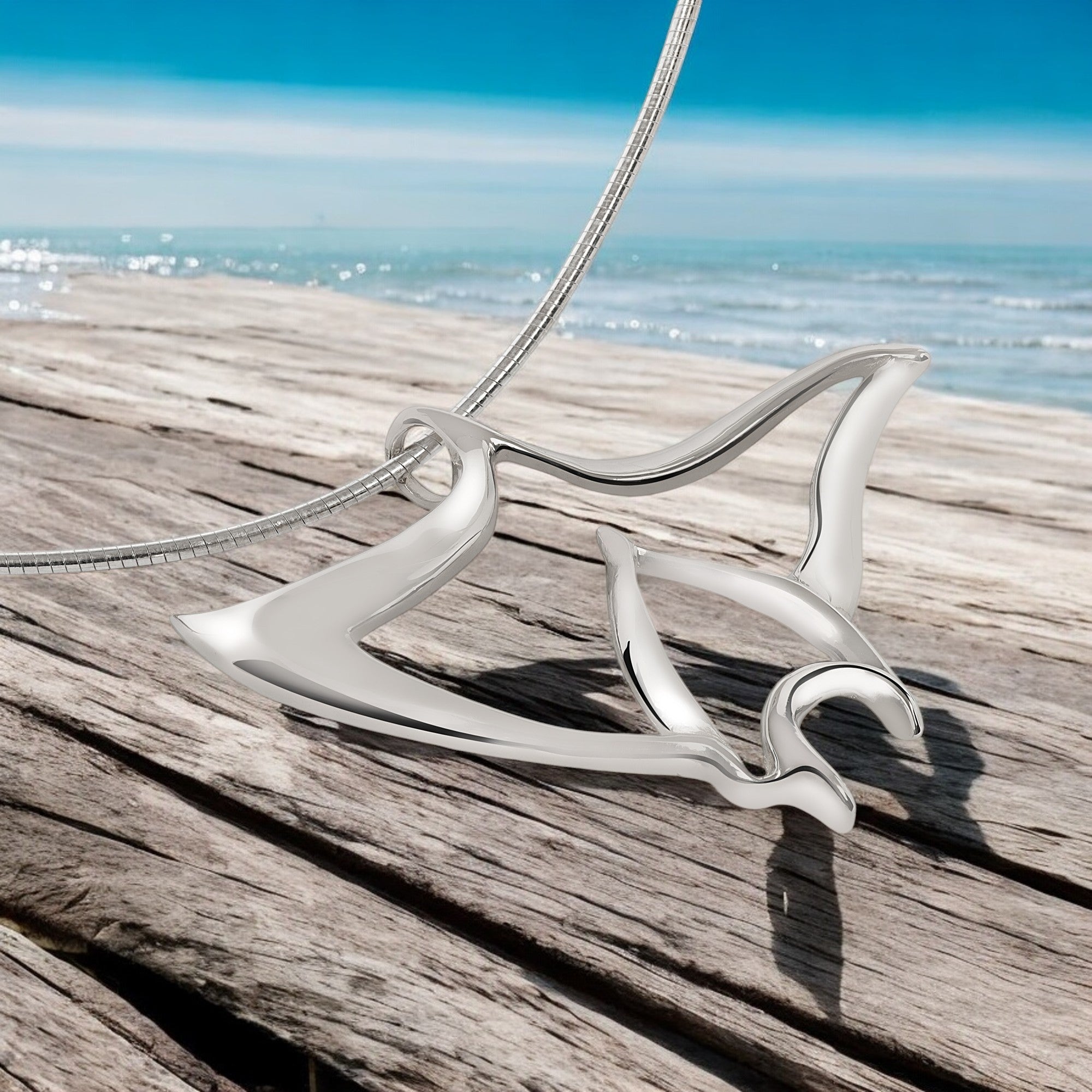 Silver necklace with a unique design on a wooden surface near water