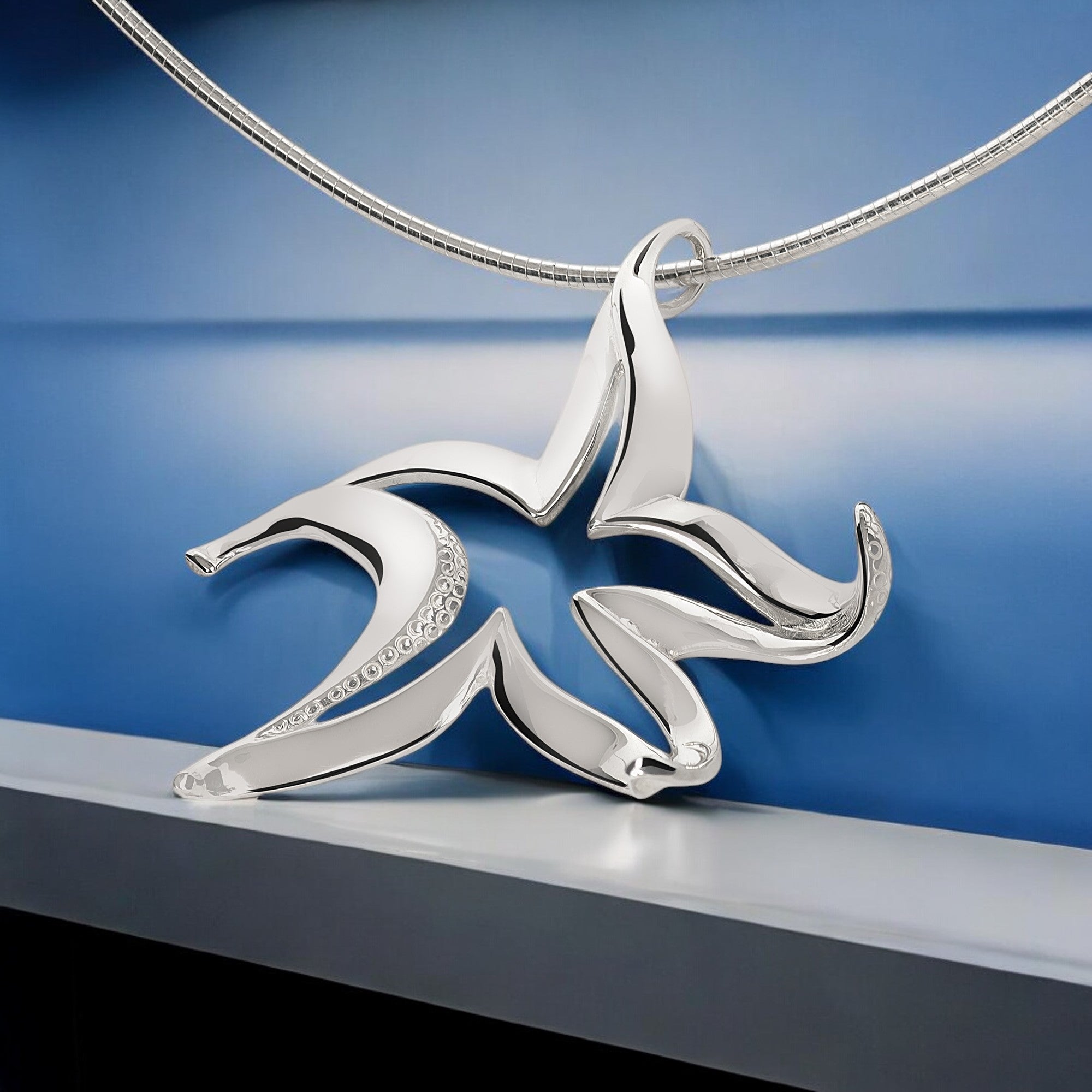 Silver necklace with a leaf-shaped pendant on a blue background