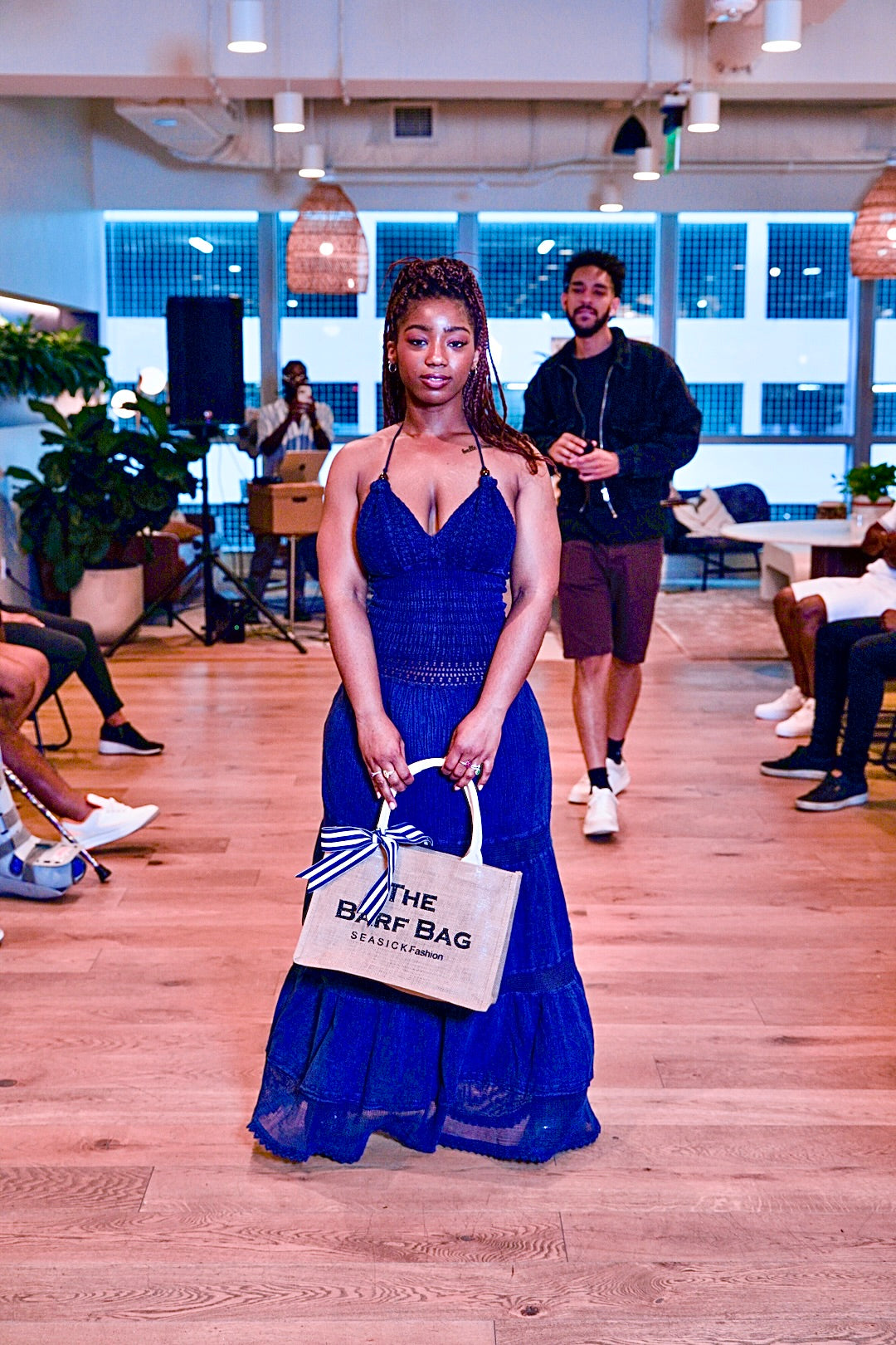 Woman in a blue dress holding a beige tote bag with text in an indoor setting.