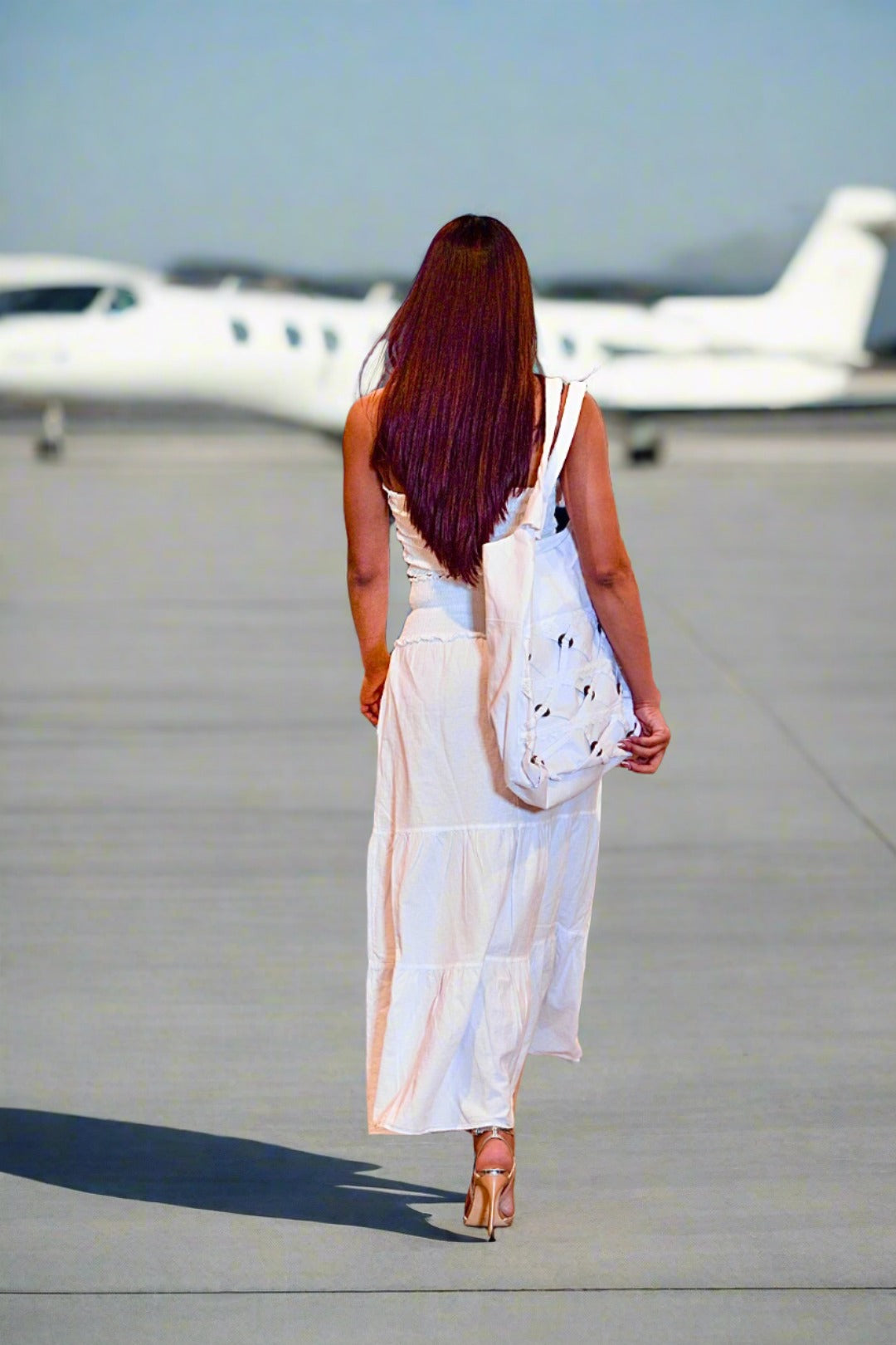 Woman in a white dress walking on an airport tarmac with airplanes in the background