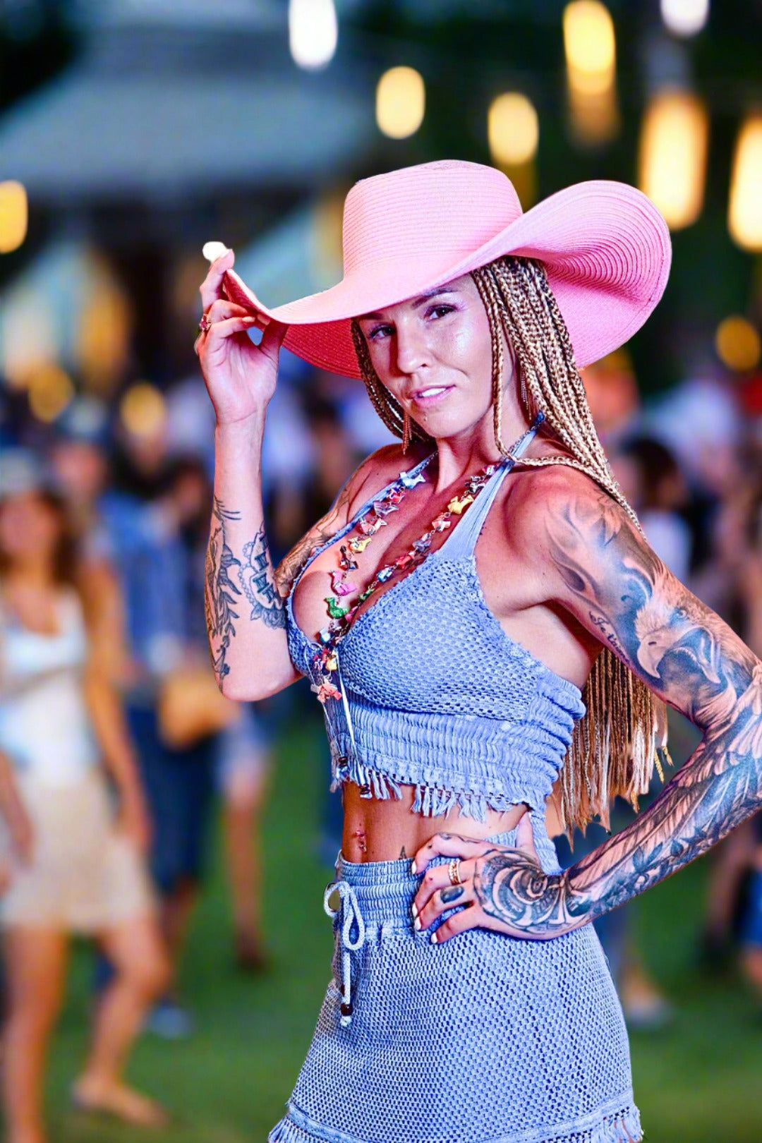 Woman wearing a pink cowboy hat and denim outfit with tattoos, standing outdoors.