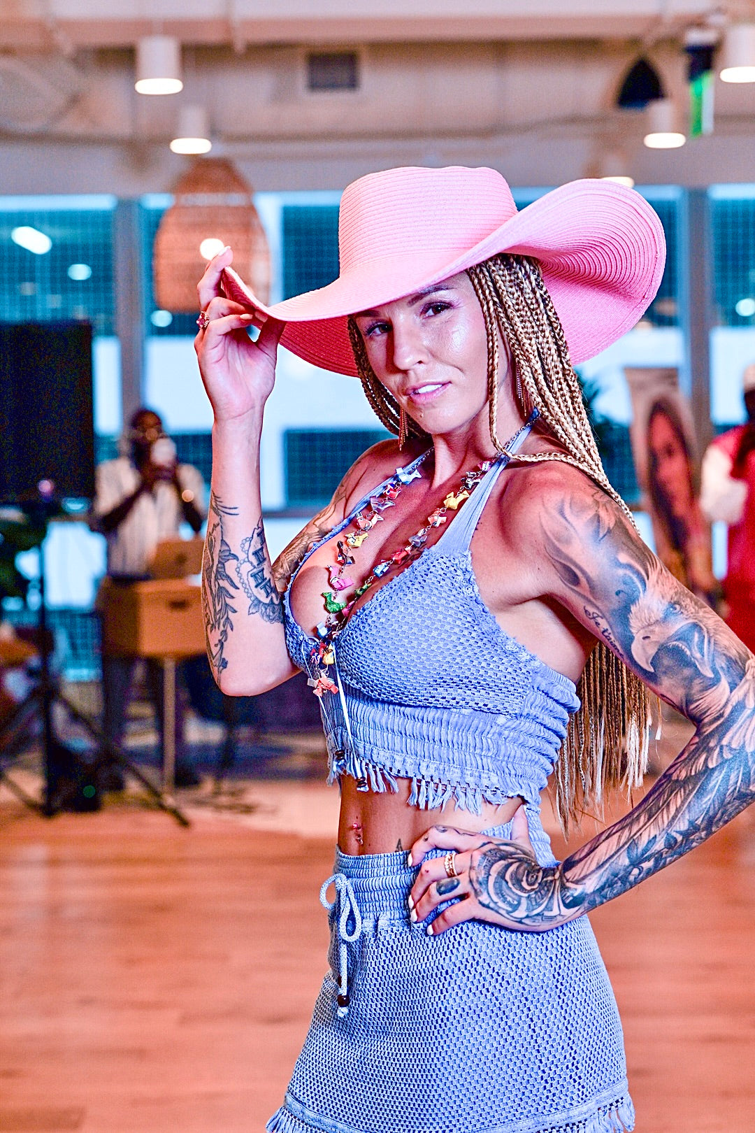Woman wearing a pink hat and blue outfit with tattoos in an indoor setting