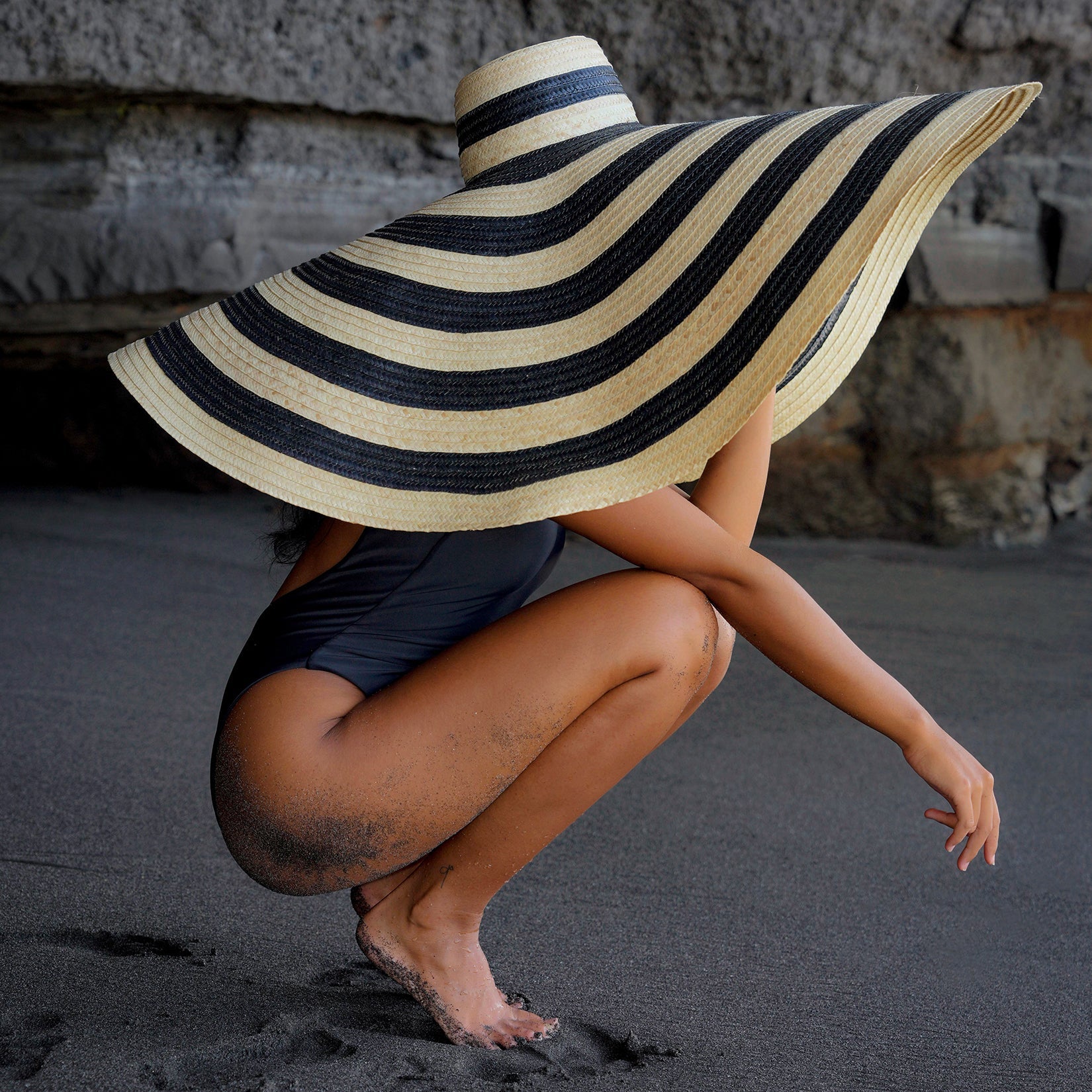 Person wearing a large striped sun hat on a beach.