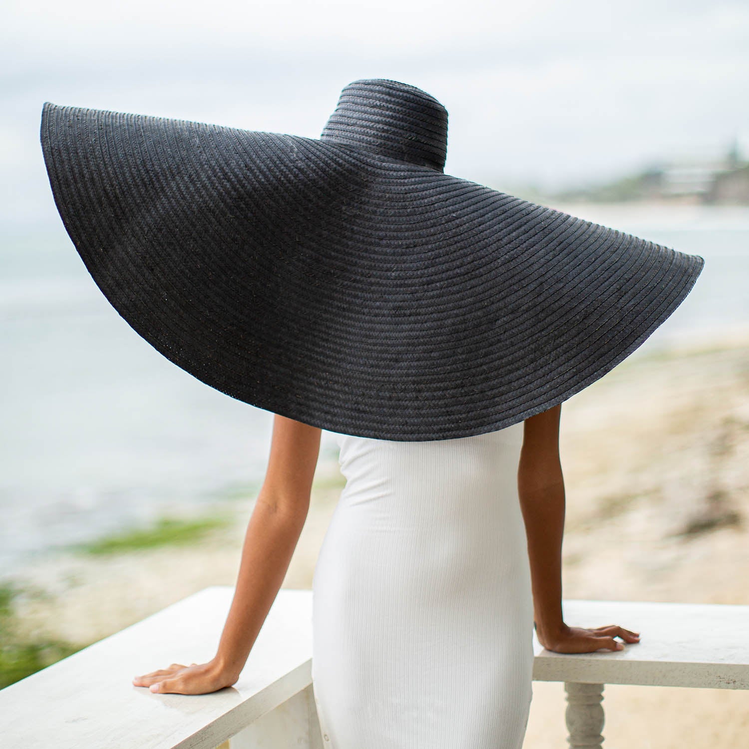 Person wearing a large black sun hat by a waterfront