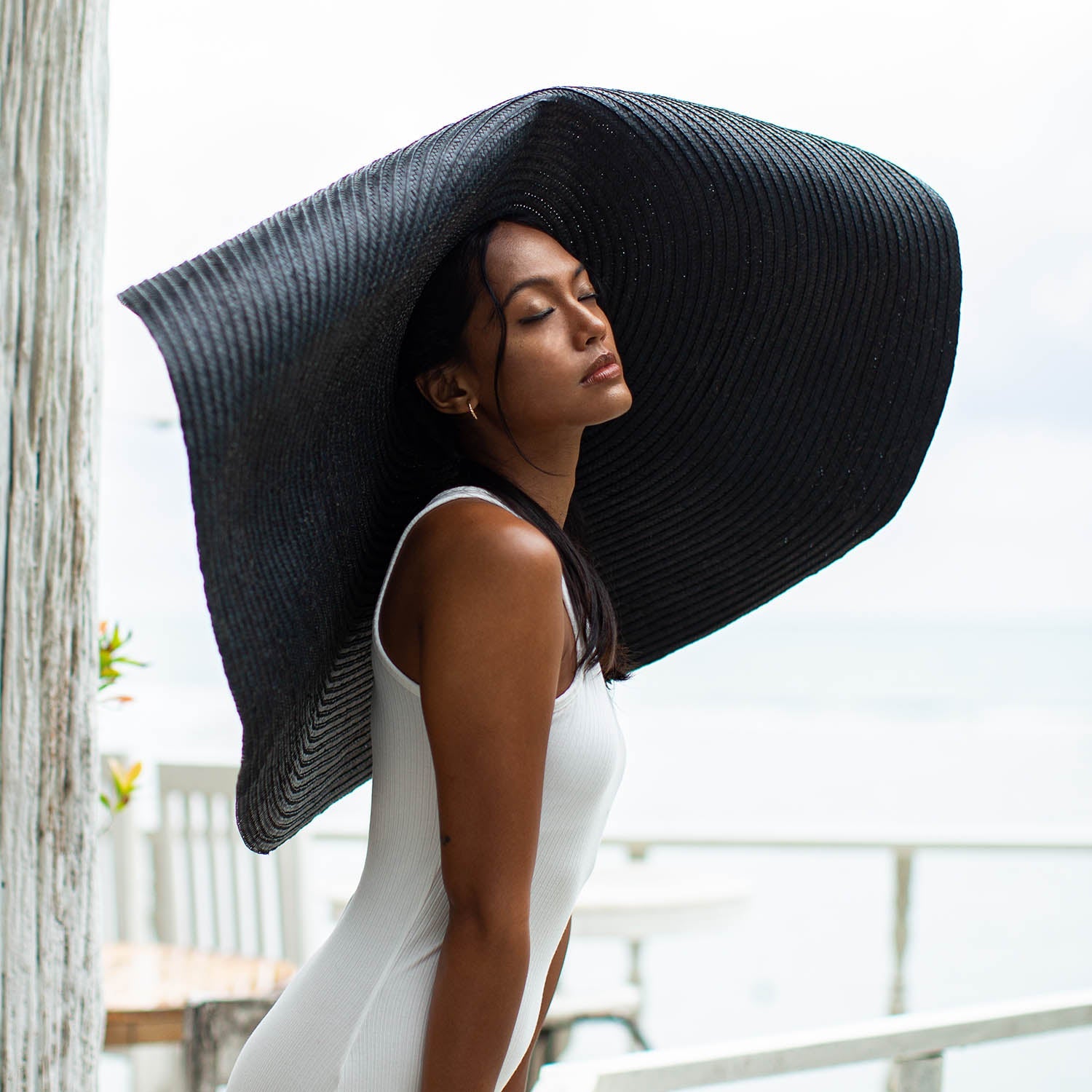 Woman wearing a large black sun hat on a blurred outdoor background