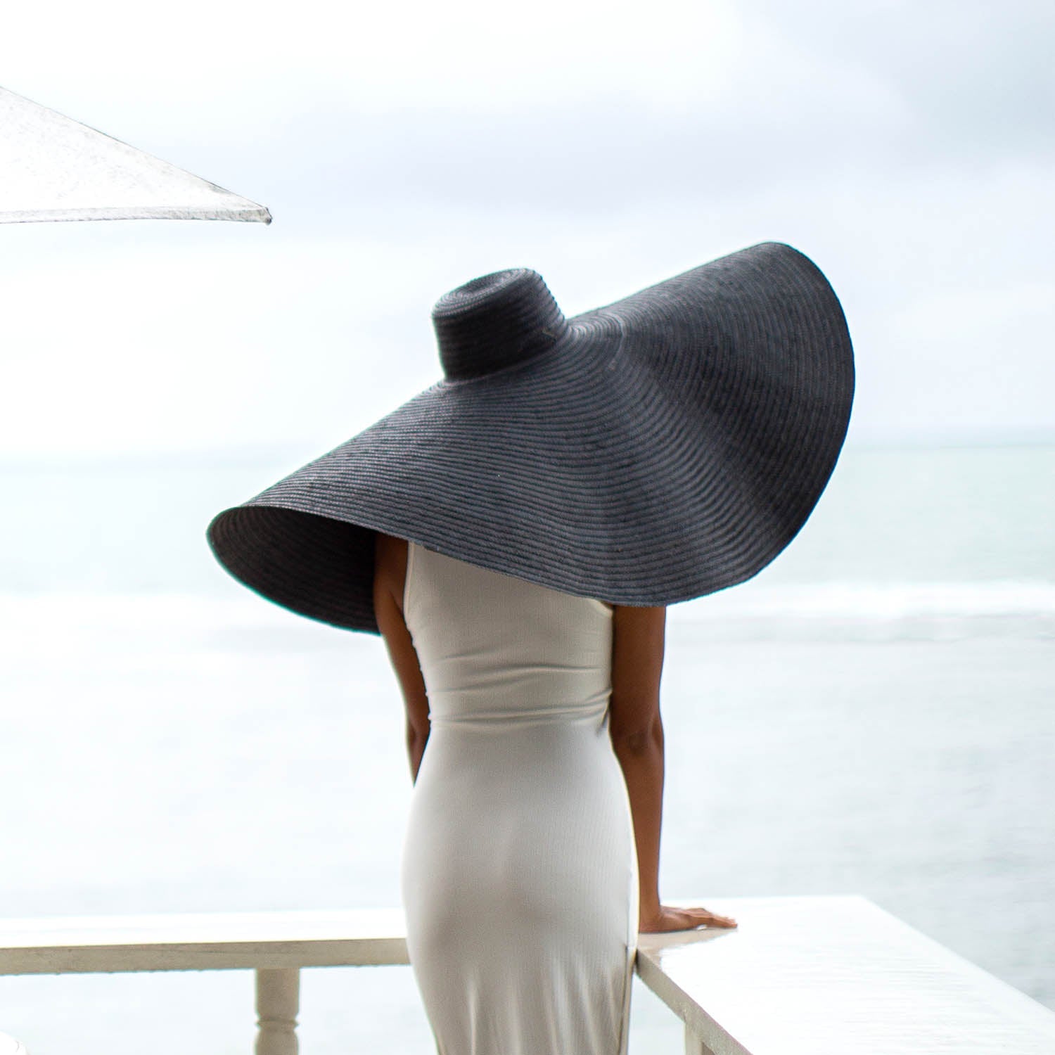 Person wearing a large black sun hat and white dress on a bright day.