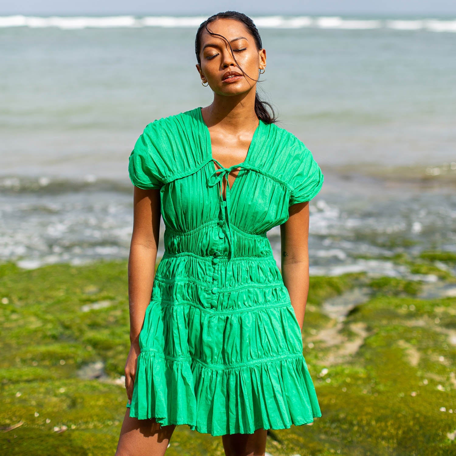Woman in a green dress standing on a beach with ocean in the background