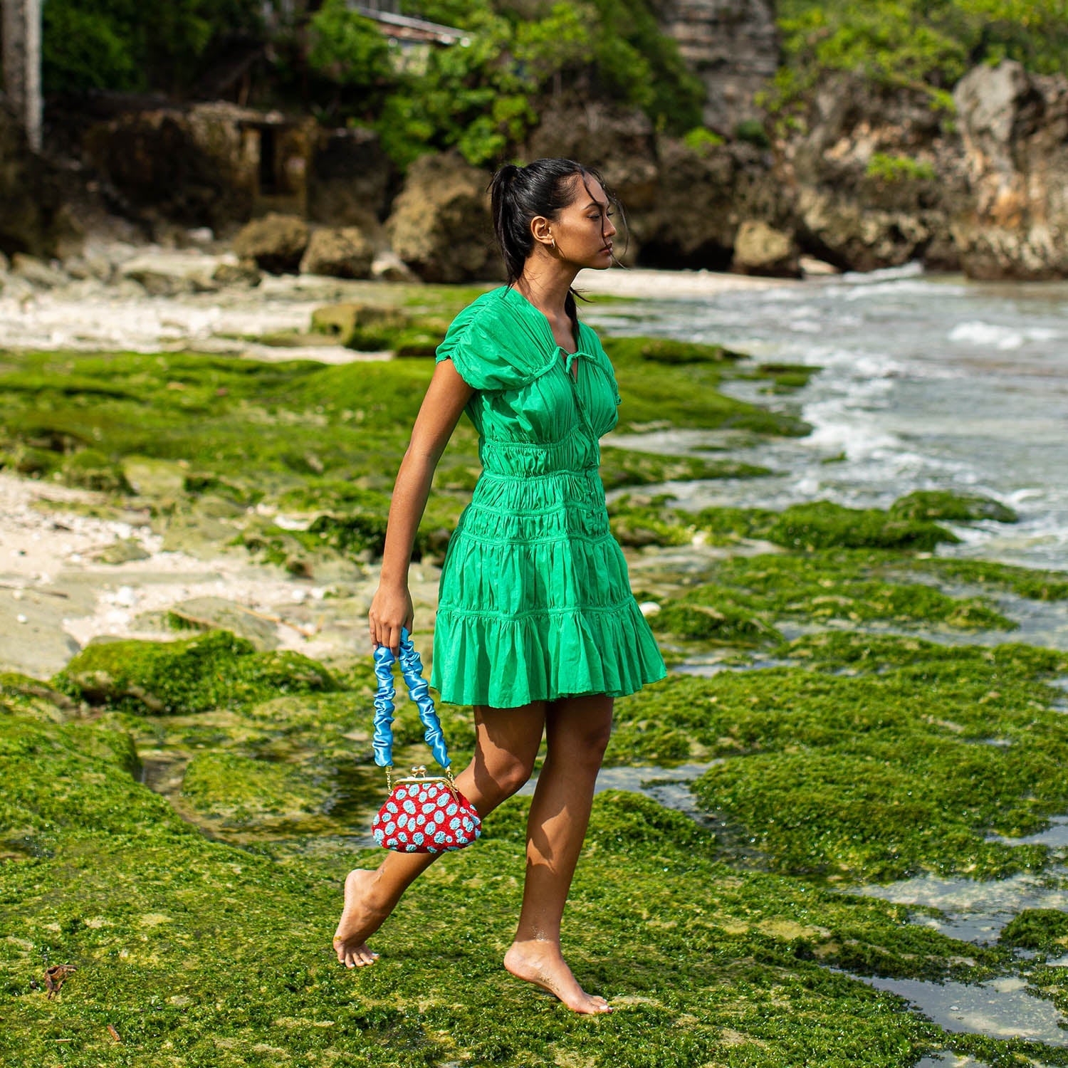 Woman in a green dress walking on a beach with green algae.