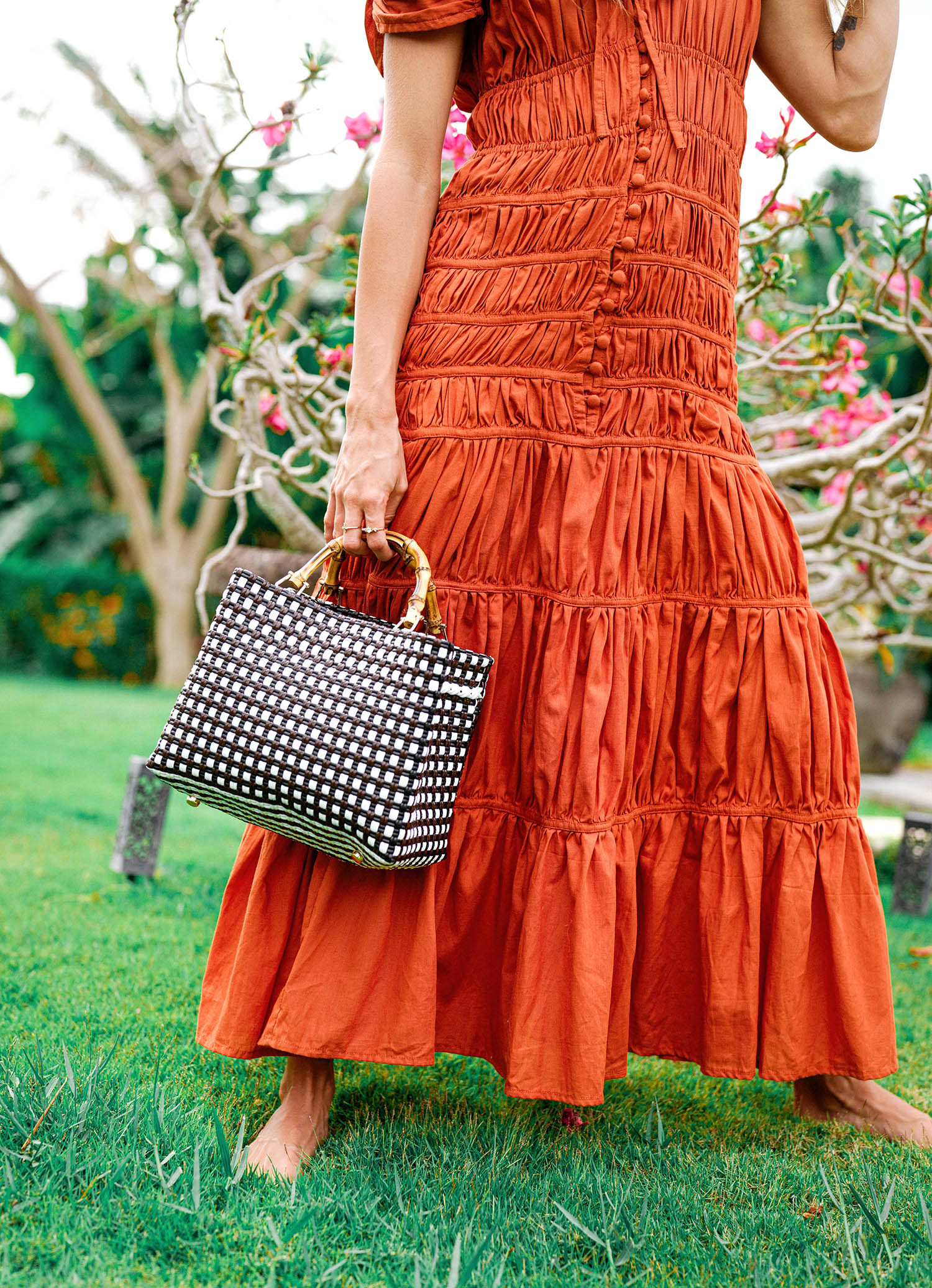 Person wearing an orange dress holding a black and white patterned handbag outdoors.