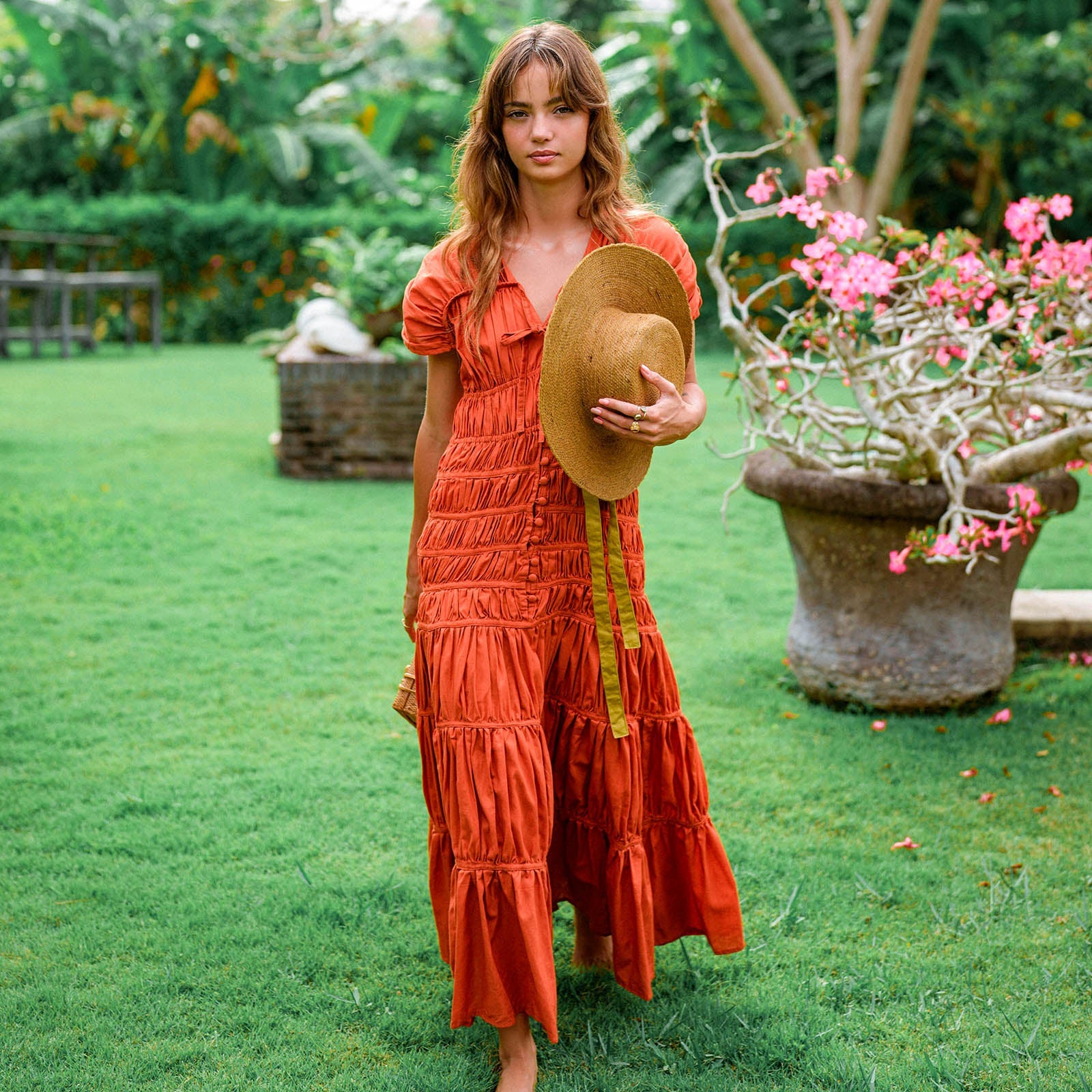 Woman in an orange dress holding a hat in a garden setting