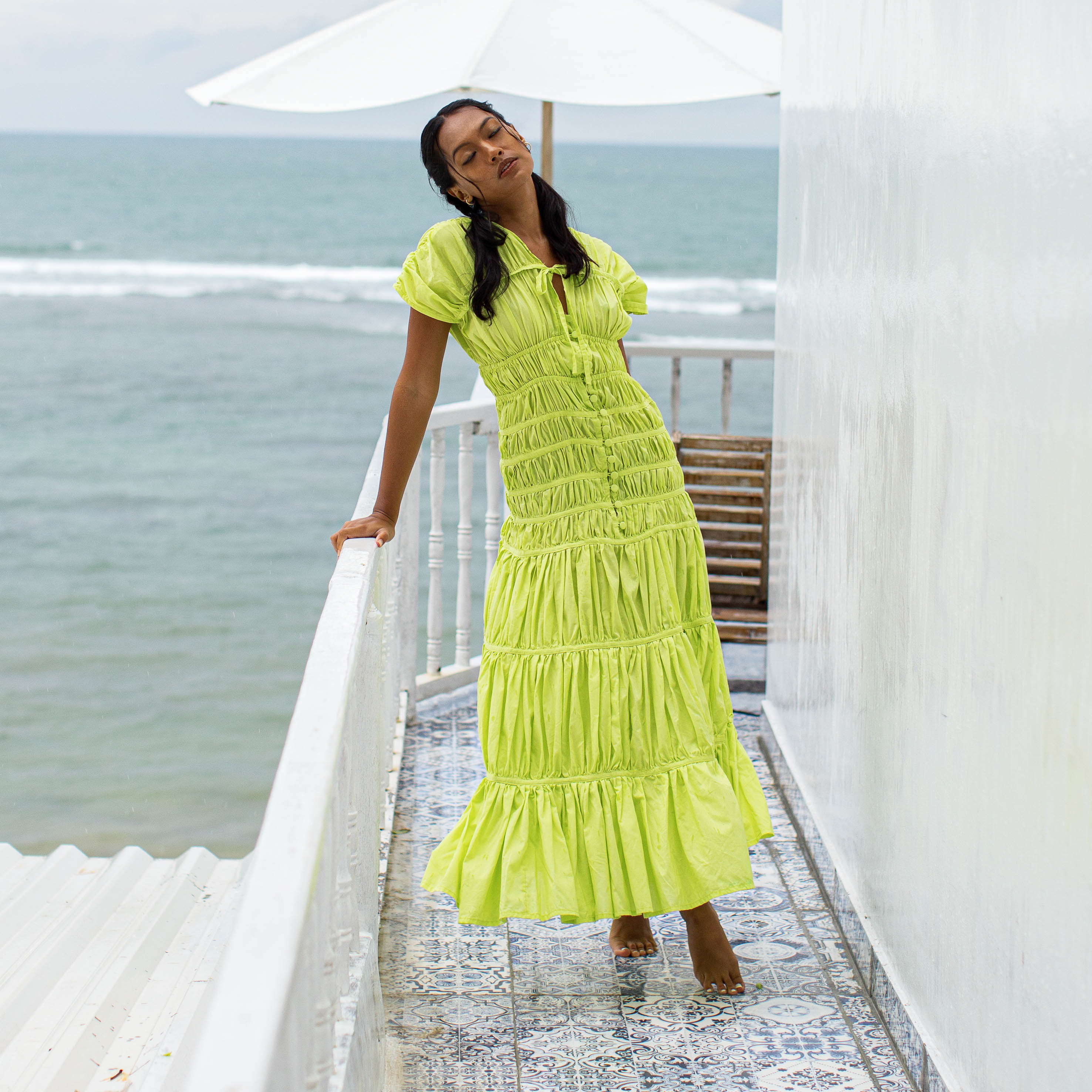 Woman in a bright yellow dress standing on a balcony with ocean view