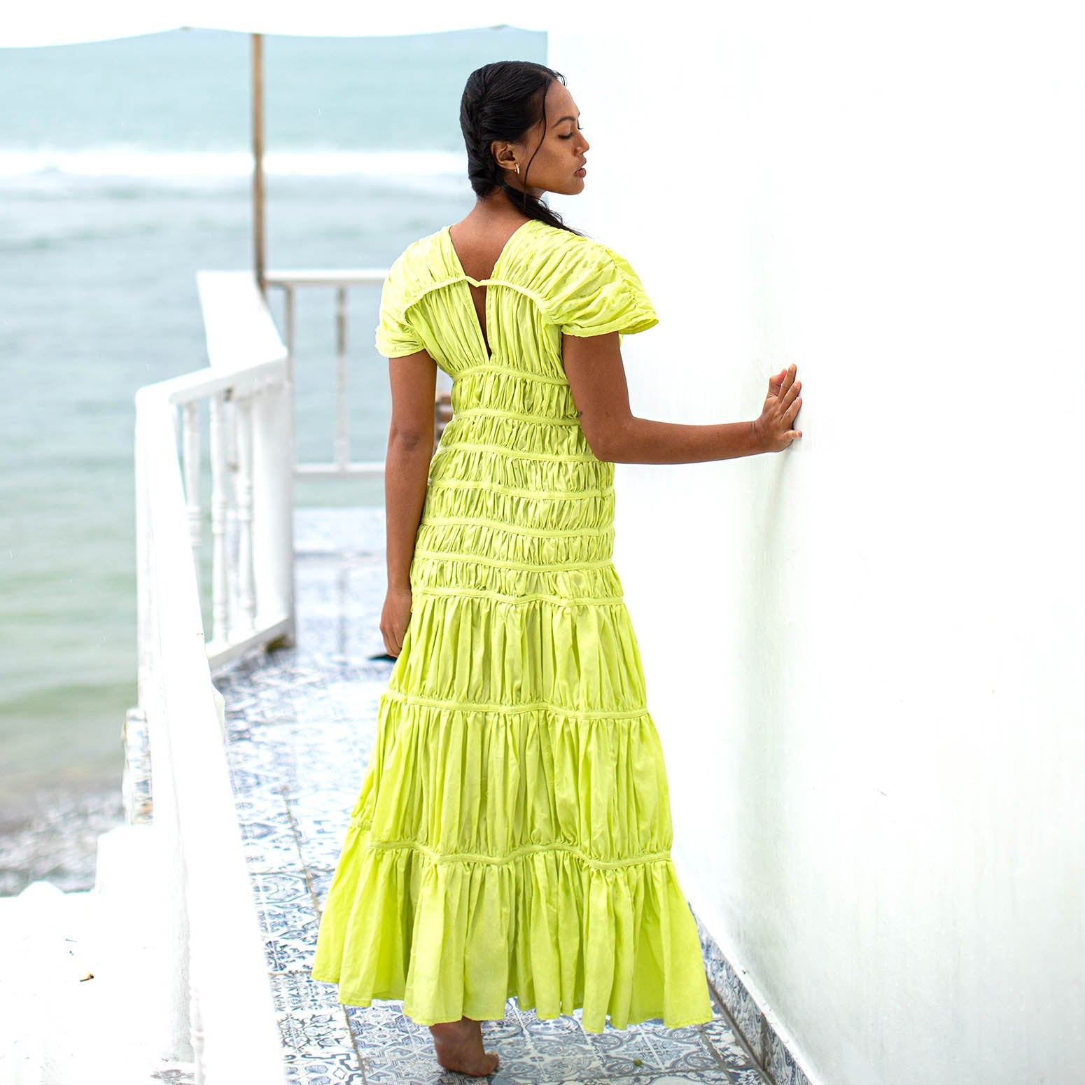 Woman in a bright yellow dress standing on a deck by the water.