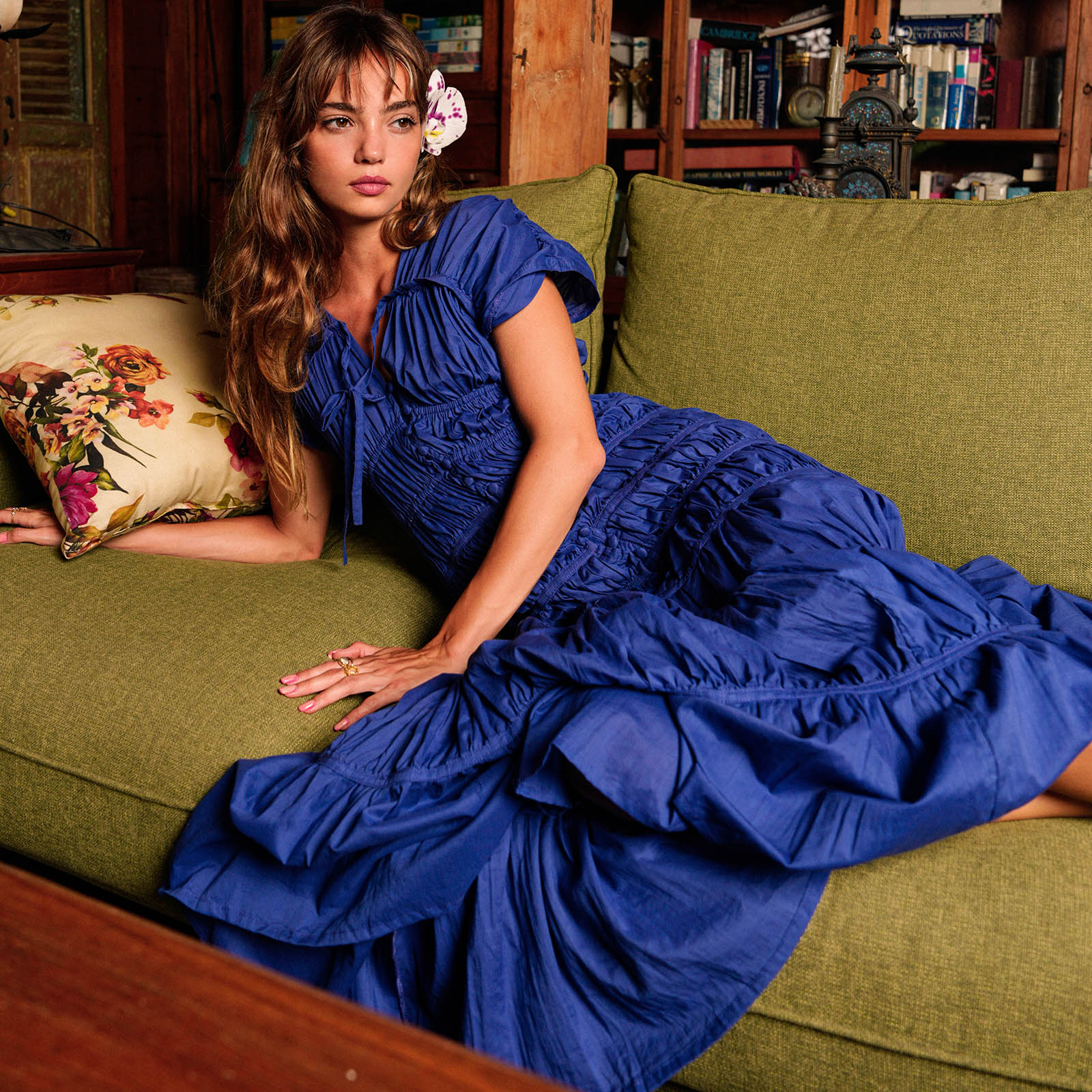 Woman in a blue dress sitting on a green couch with a floral pillow.