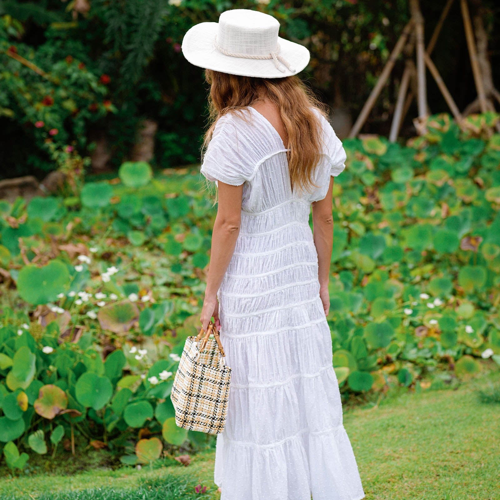 Woman in a white dress and hat walking through a garden