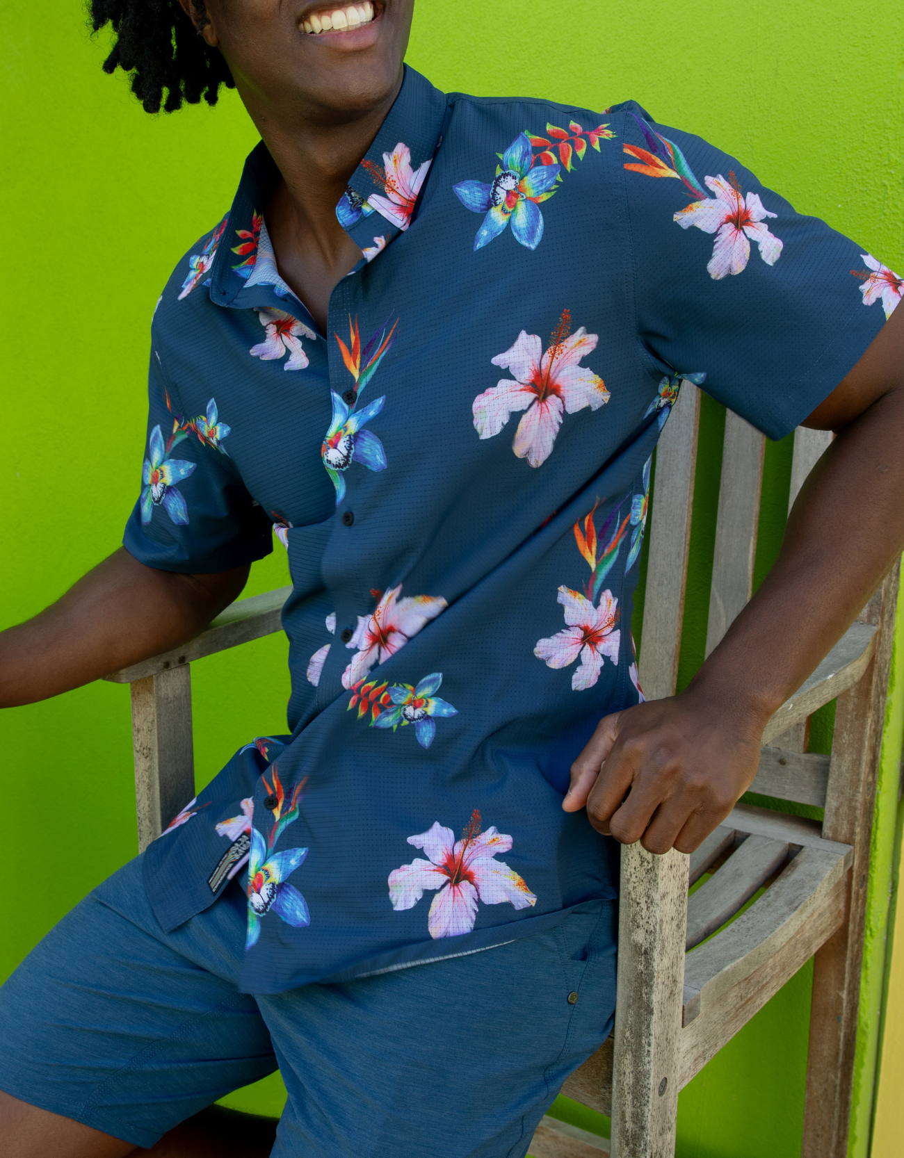 Person wearing a navy blue floral shirt and shorts against a green background