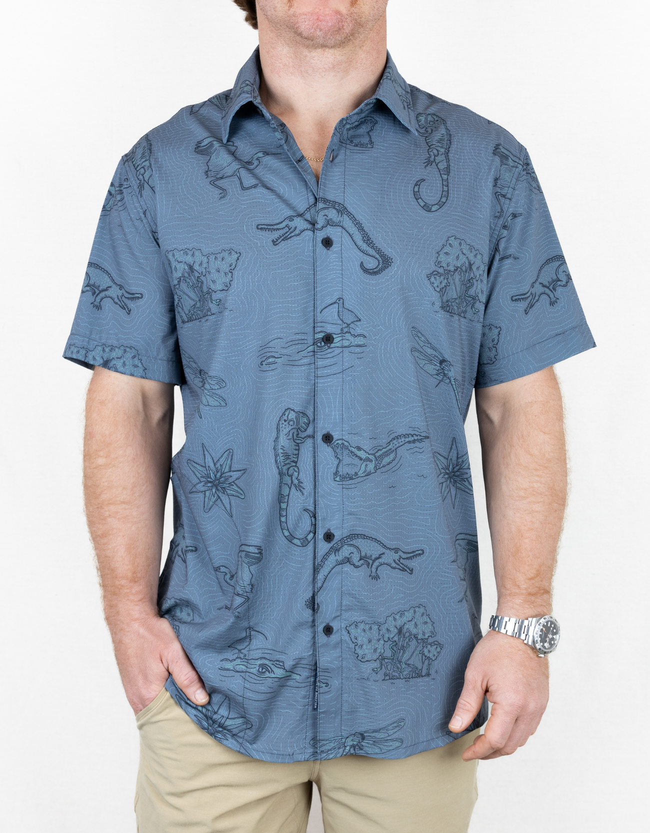 Man wearing a blue patterned shirt with beige pants on a white background