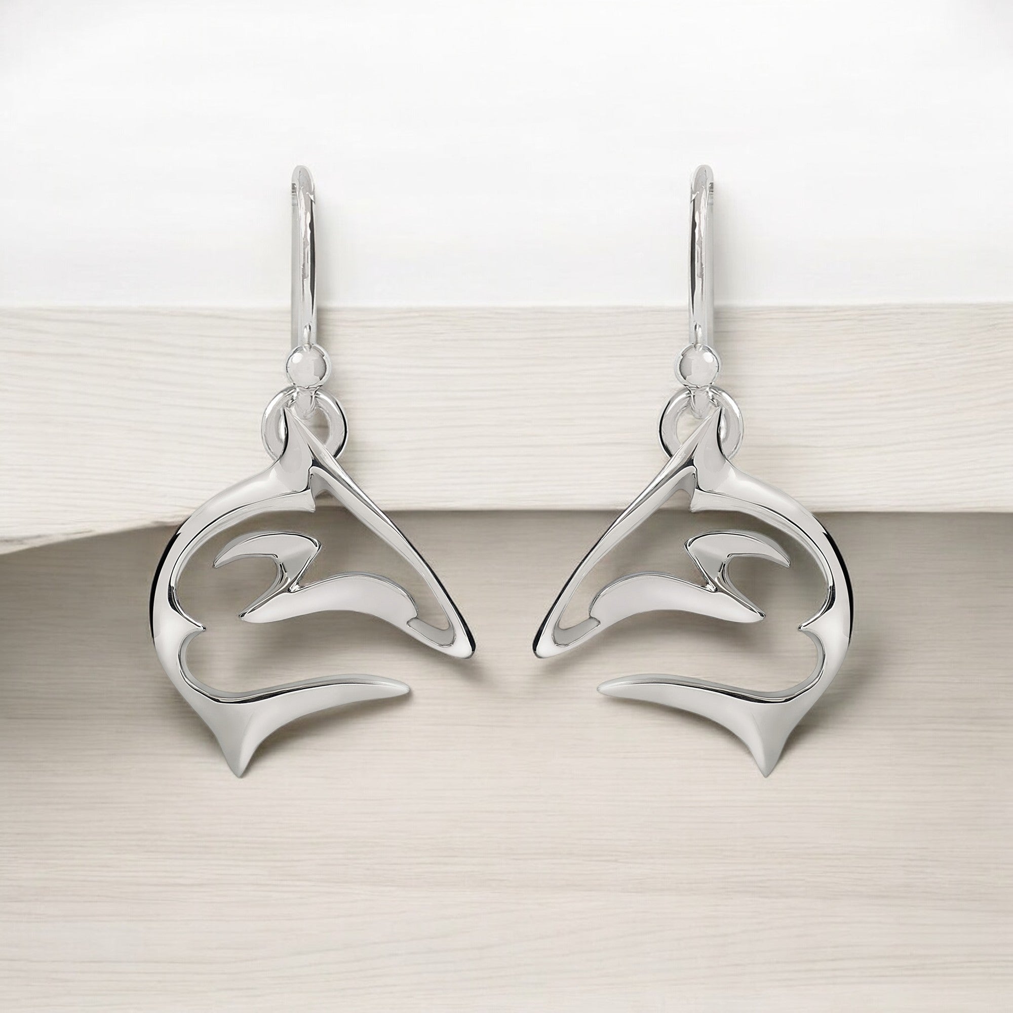 Pair of silver dolphin-shaped earrings on a light wooden surface.