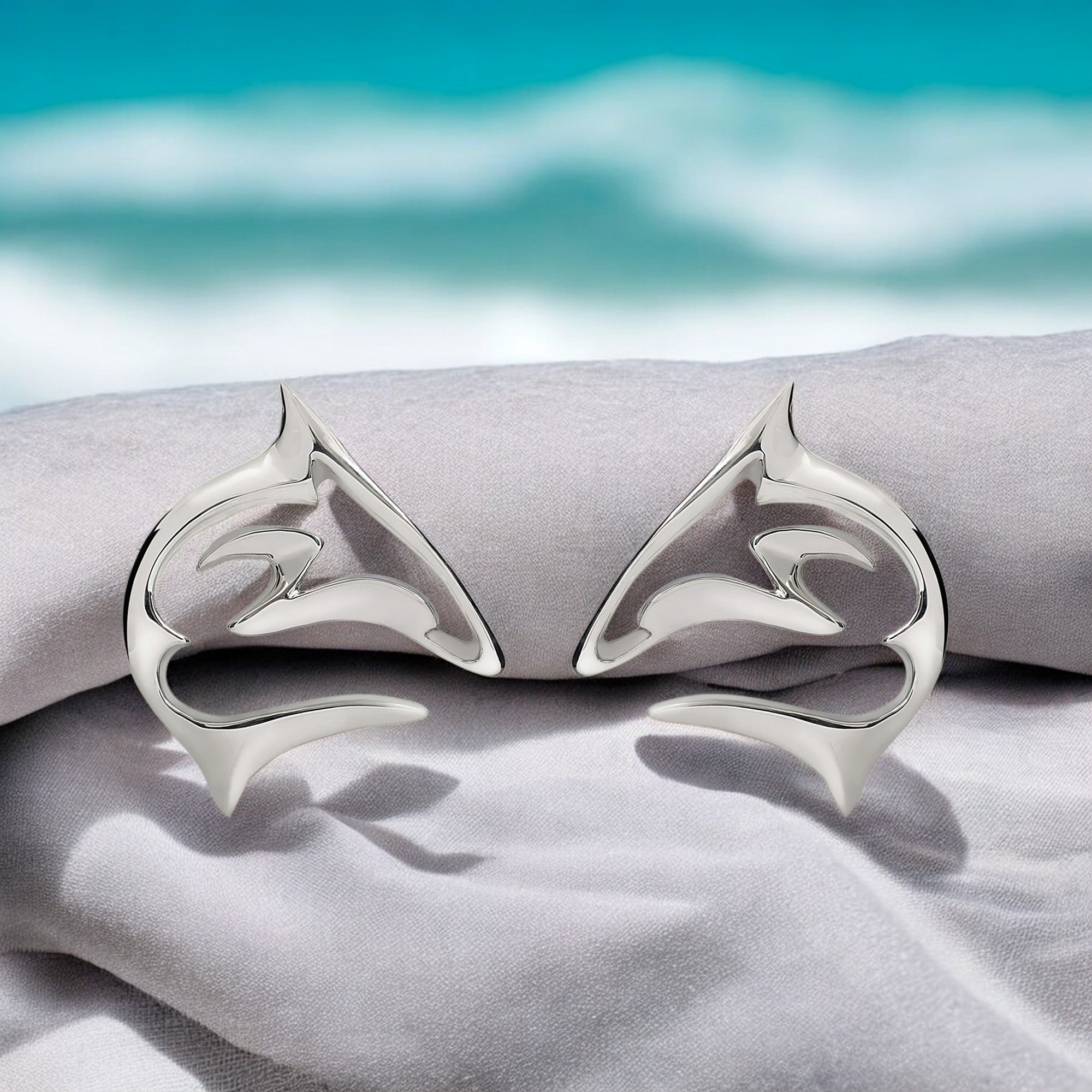 Silver bat-shaped earrings on a textured surface with a blurred beach background