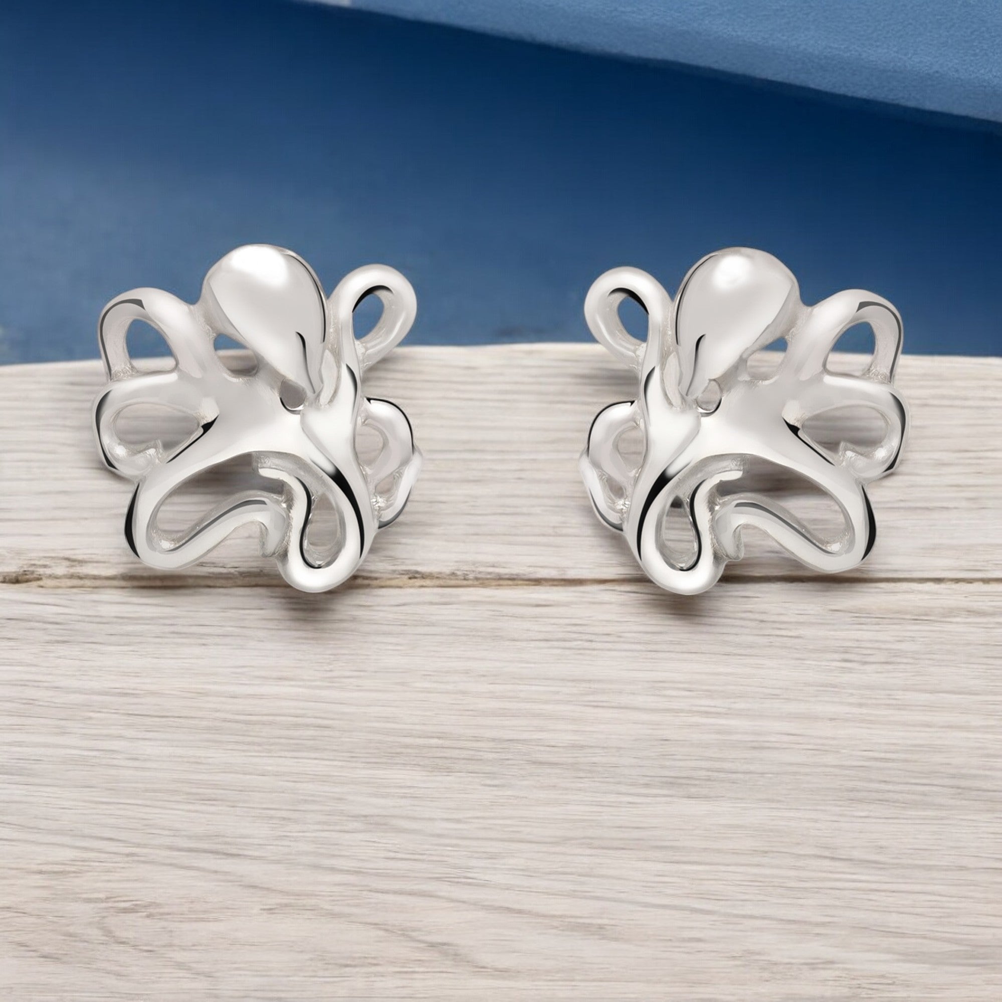 Pair of silver octopus-shaped earrings on a wooden surface with a blue background