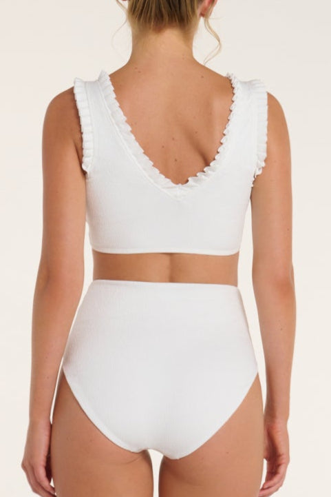 White bikini set with ruffled details on a beige background