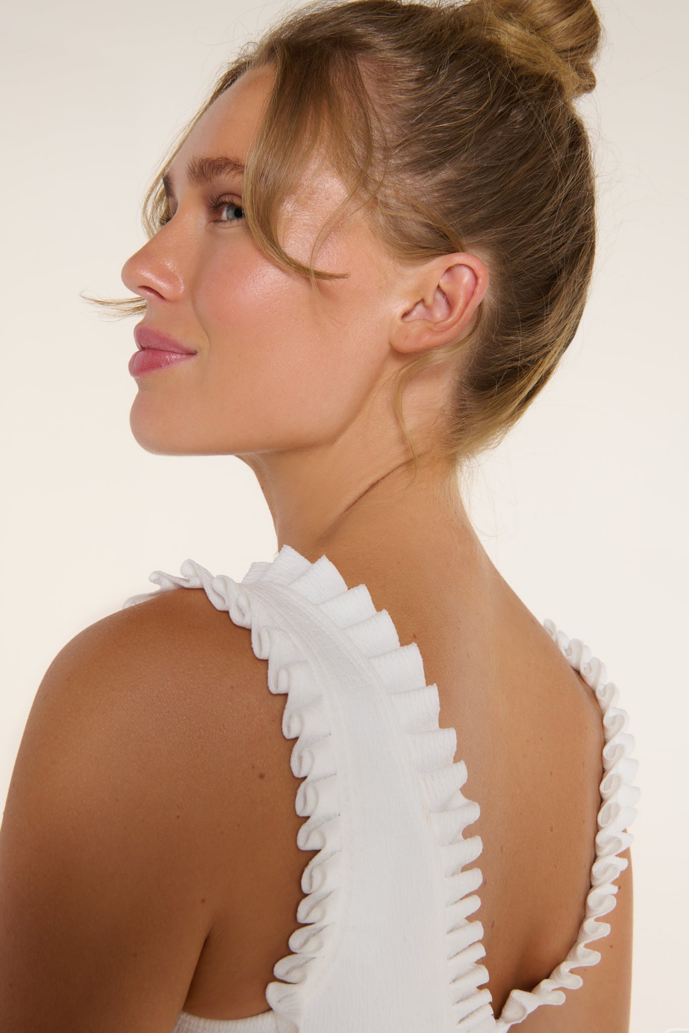 Woman wearing a white dress with ruffled straps against a plain background